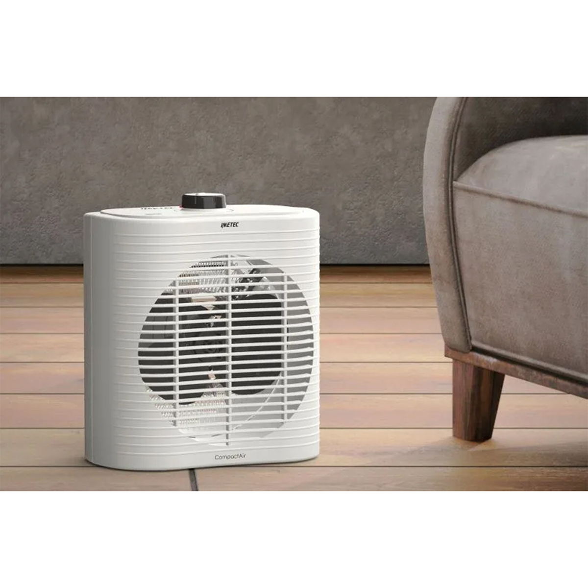 Biały kompaktowy grzejnik wentylatorowy. Czarne górne sterowanie. Wnętrze z drewnianą podłogą i krzesłem.