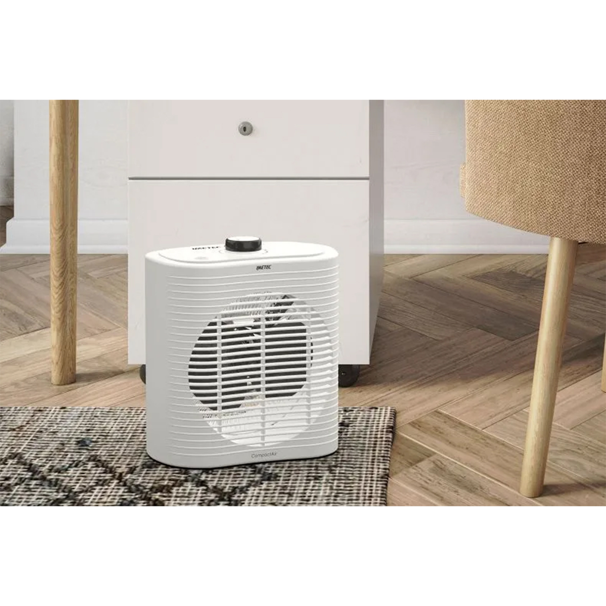 Biały grzejnik wentylatorowy na podłodze z dywanikiem, obok białej szafki i drewnianych nóg.