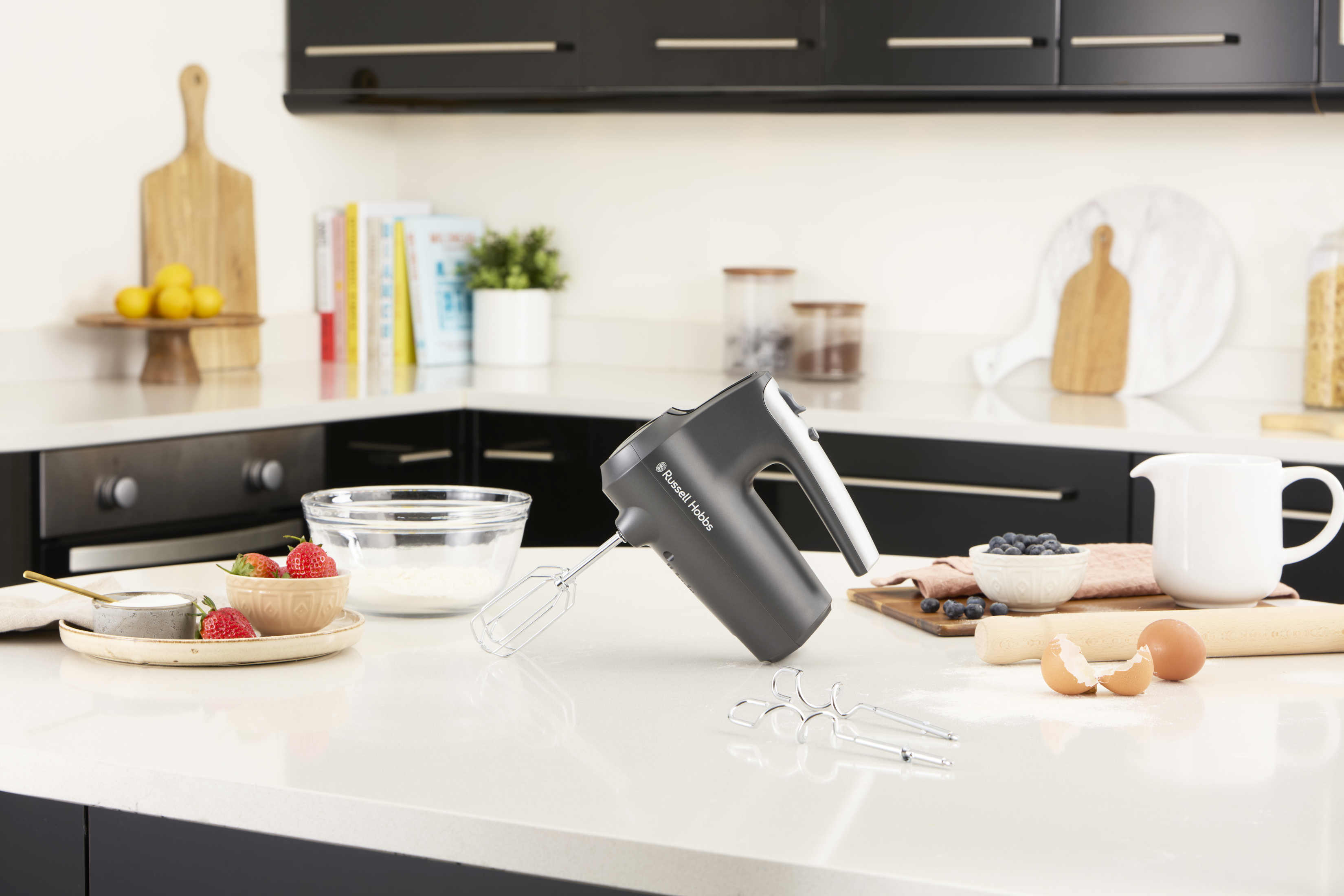 Scena kuchenna z szarą mikserem ręcznym na białym blacie, plus składniki i przybory.