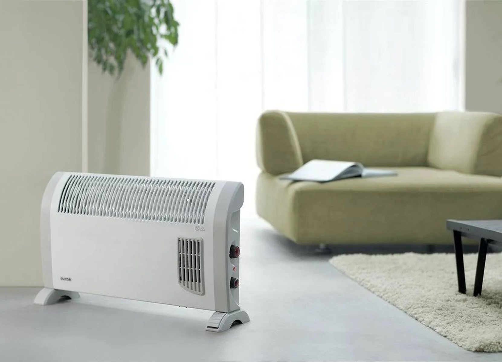Ein weißer Elektroheizer steht in einem Wohnzimmer mit Sofa und Teppich.