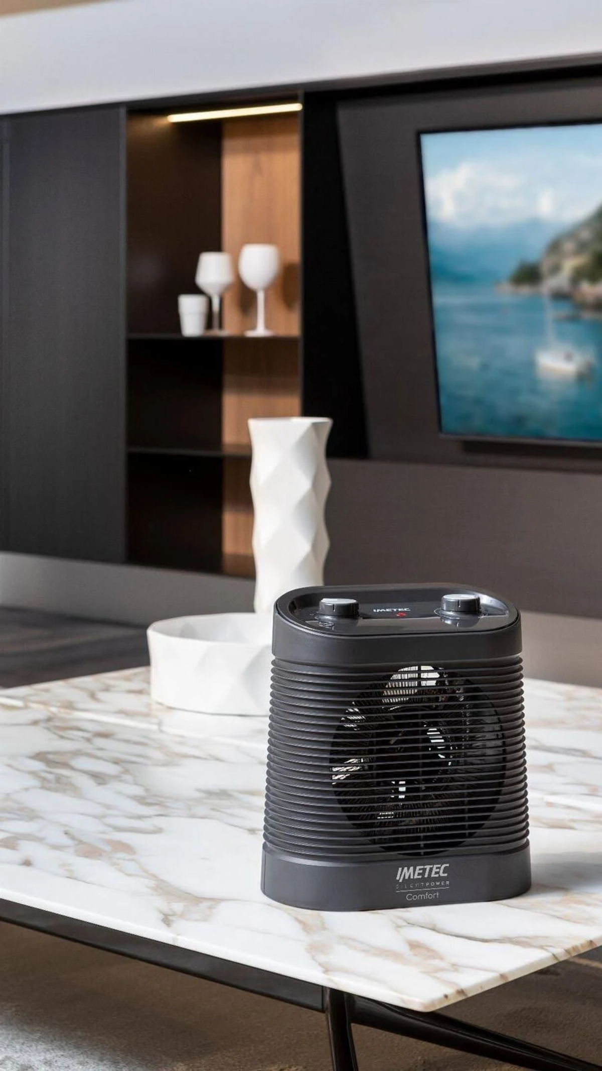 Czarny grzejnik Immetec na marmurowym stole, białe dekoracje i TV w tle.