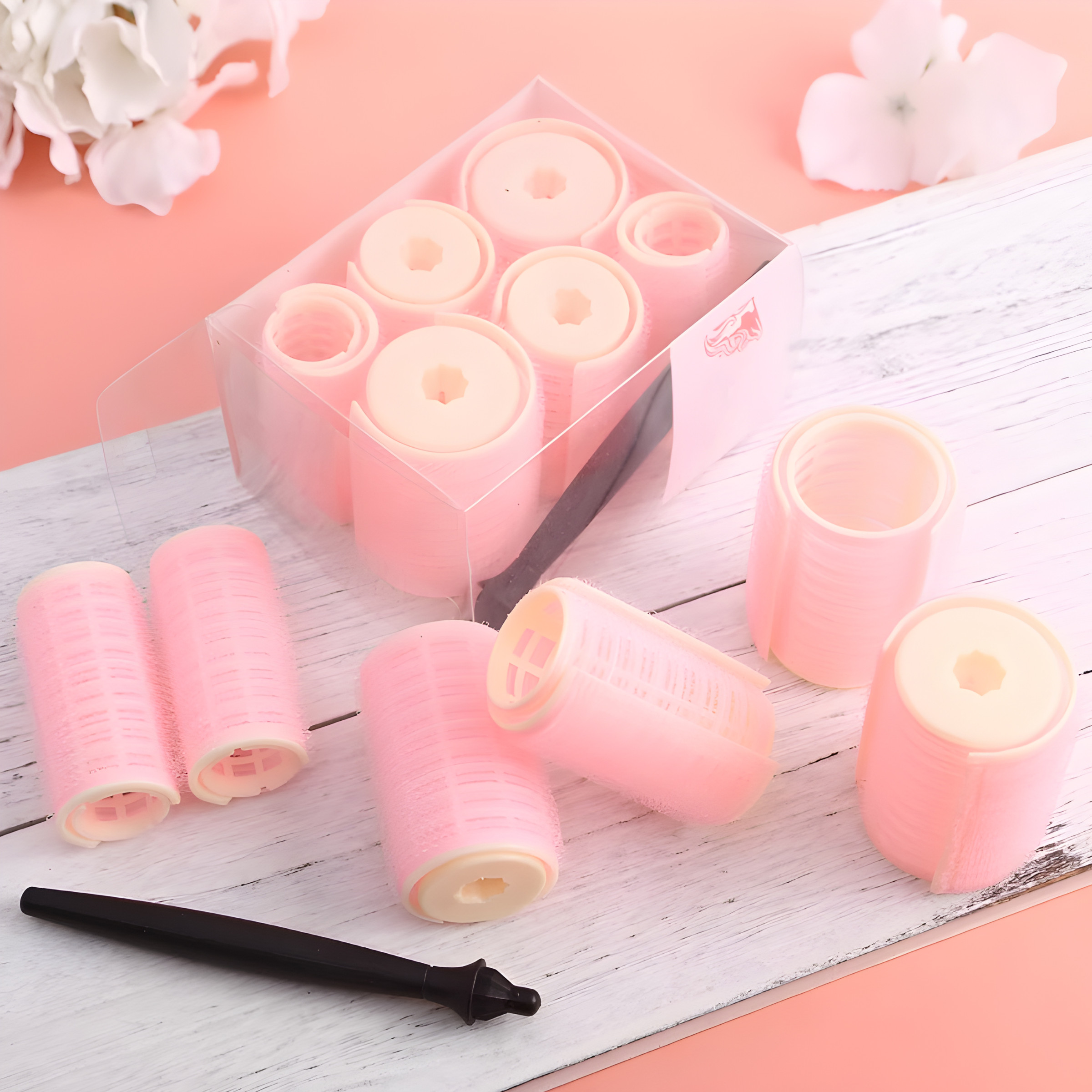 Rosa Lockenwickler in einer transparenten Box, mit Styling-Tools auf einer rosa Holzoberfläche. Kosmetikwerkzeuge.