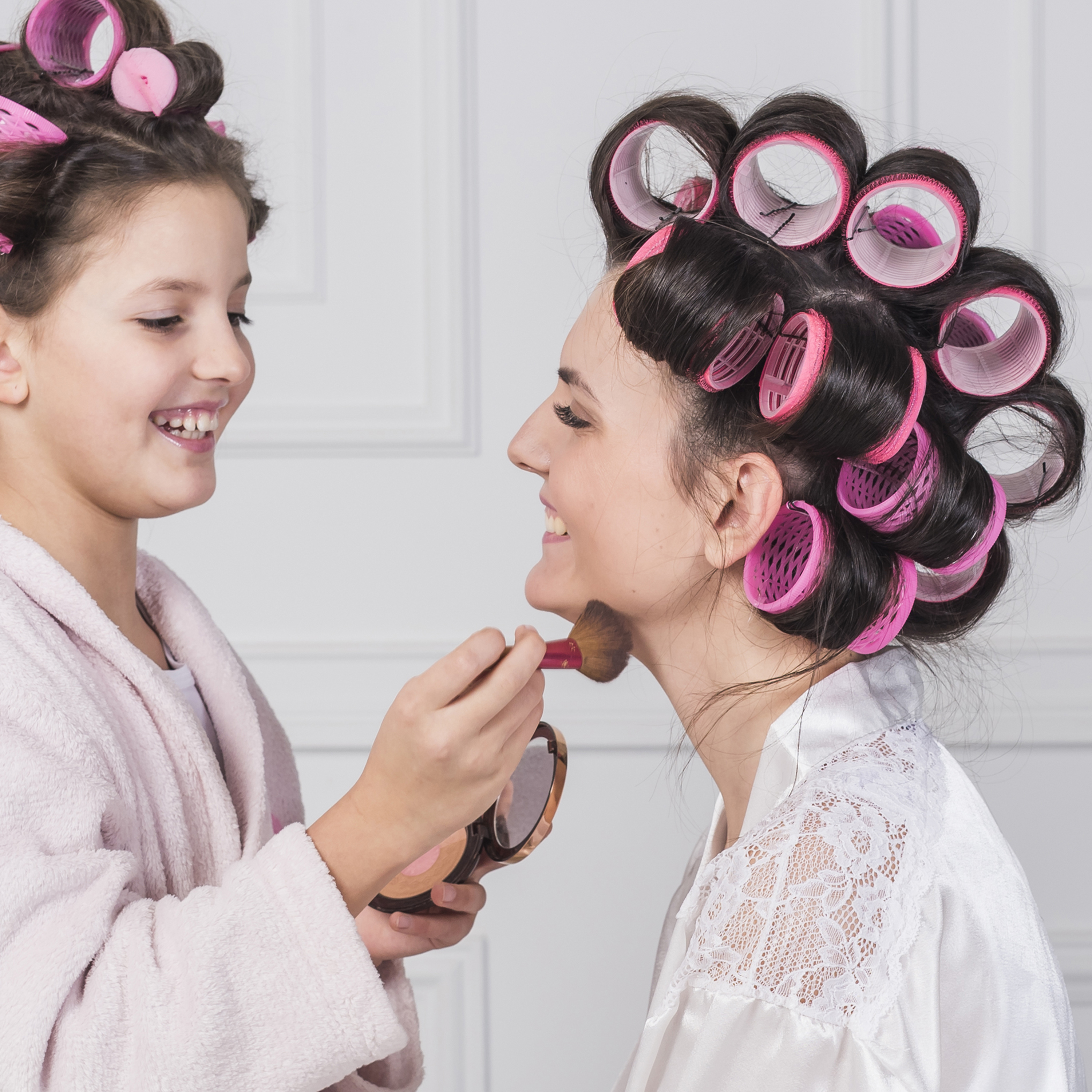 Ein Mädchen trägt Make-up auf eine Frau mit Lockenwicklern im Haar auf.