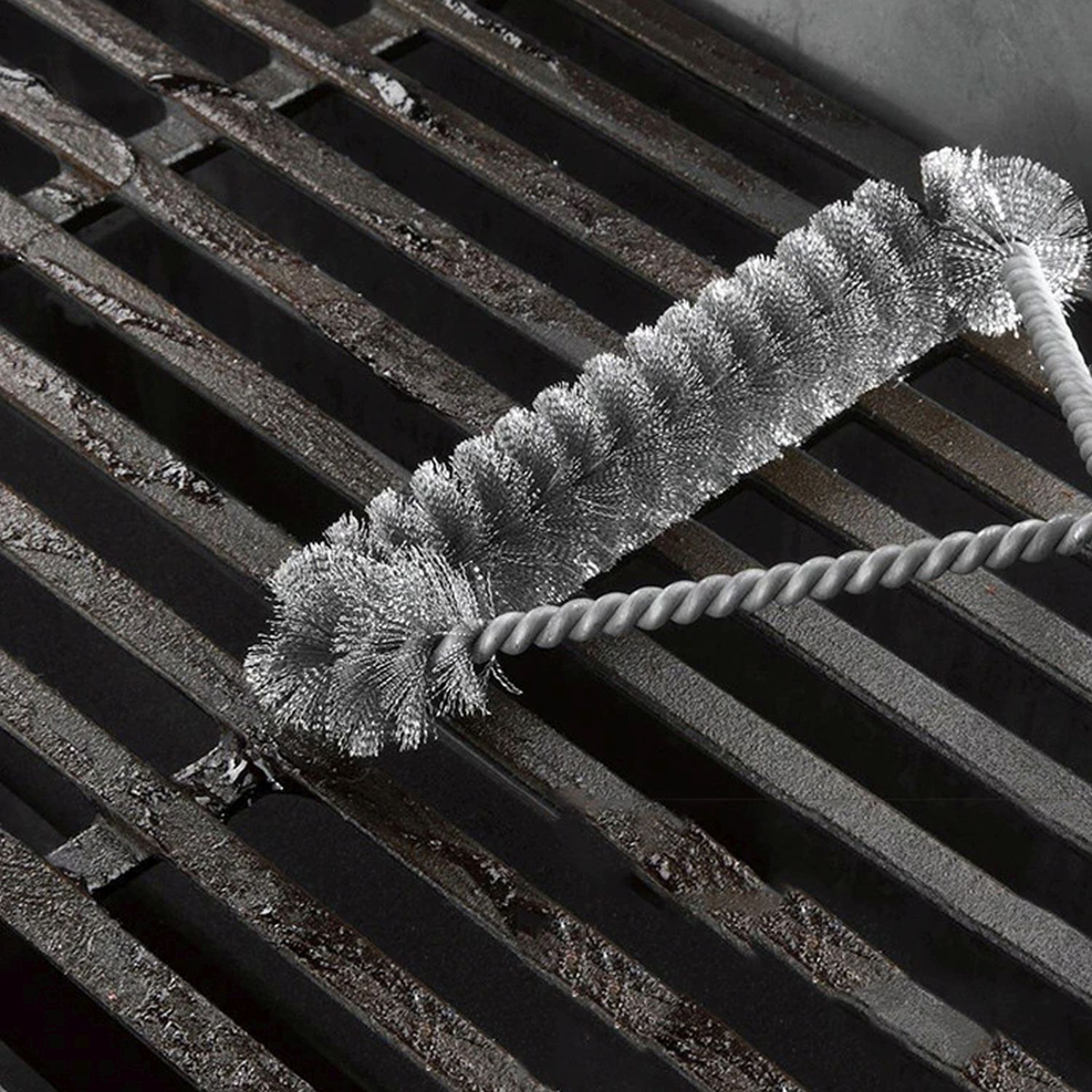 Eine Grillbürste, die einen Grill reinigt. Die Bürste ist silberfarben und hat einen gedrehten Drahtgriff.
