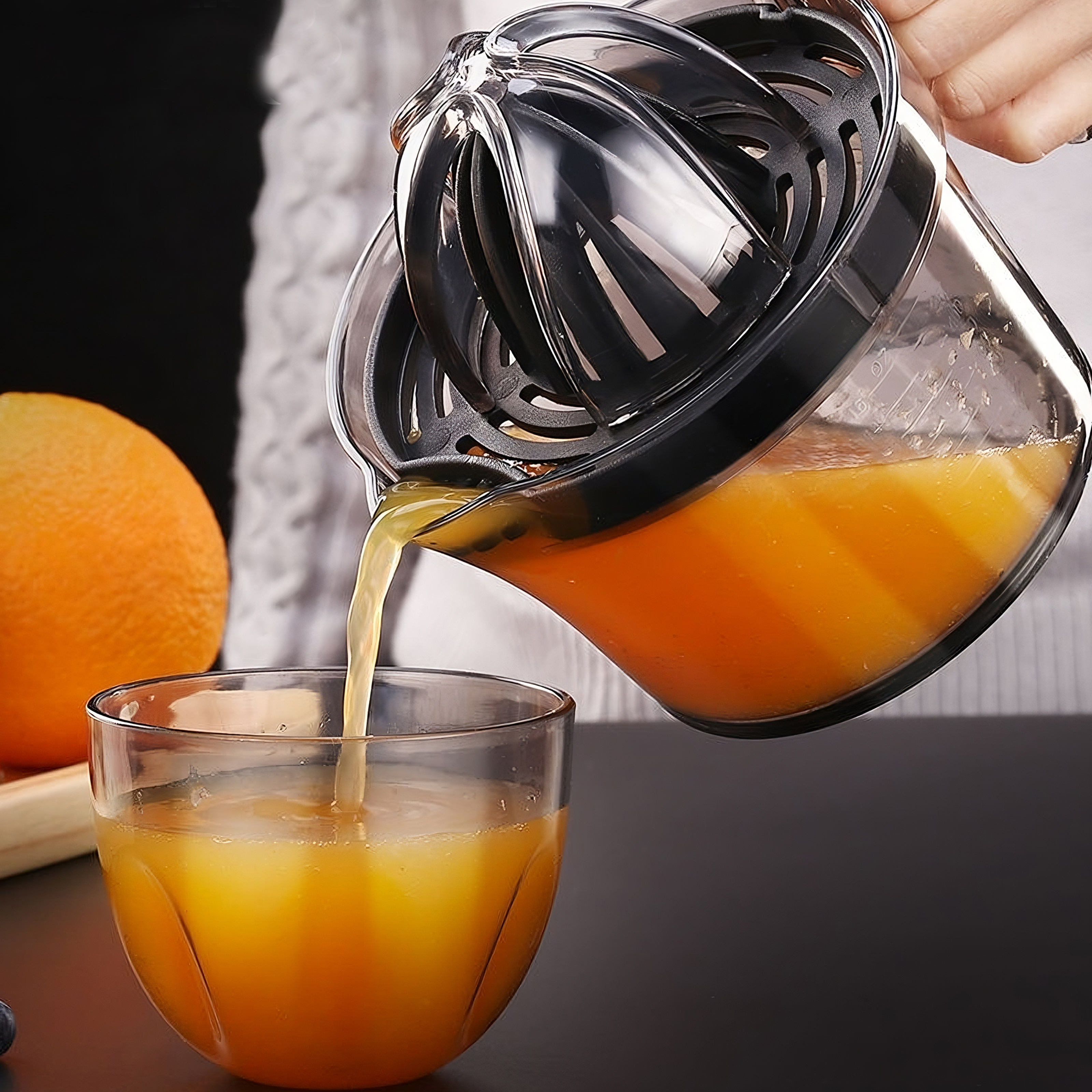 Saft wird aus einem Entsafter in ein Glas gegossen. Eine Orange ist im Hintergrund sichtbar.
