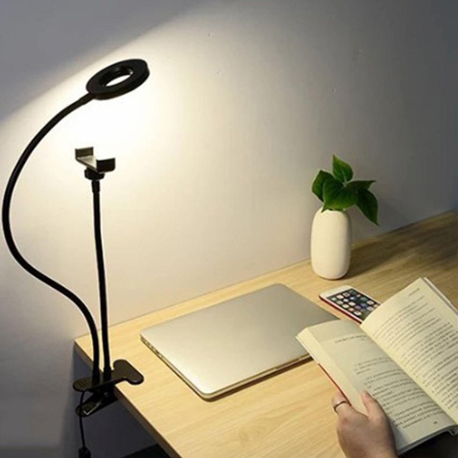 Ein Schreibtisch mit Lampe, Telefon, Buch und Laptop. Eine Hand blättert im Buch.