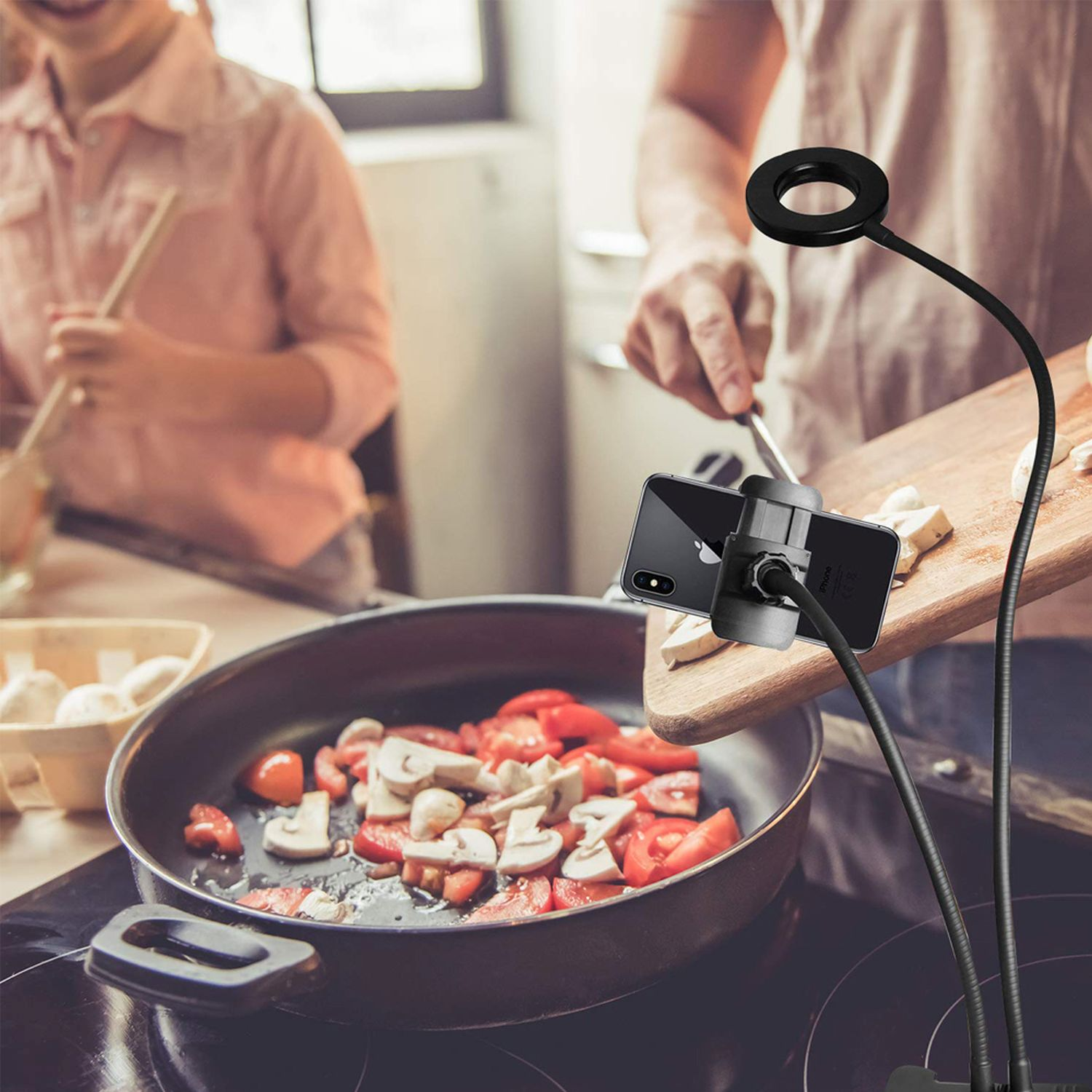 Leute kochen mit Smartphone auf flexiblem Arm mit Ringlicht, über einer Pfanne.