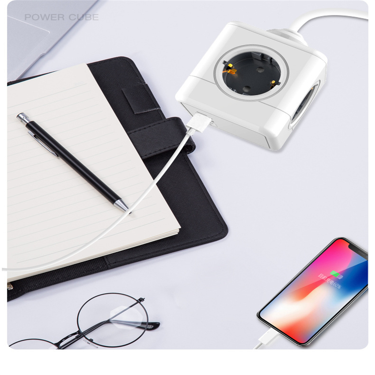 Ein Power Cube, Notizbuch, Stift, Brille und Telefon werden aufgeladen. Alles auf weißer Oberfläche.