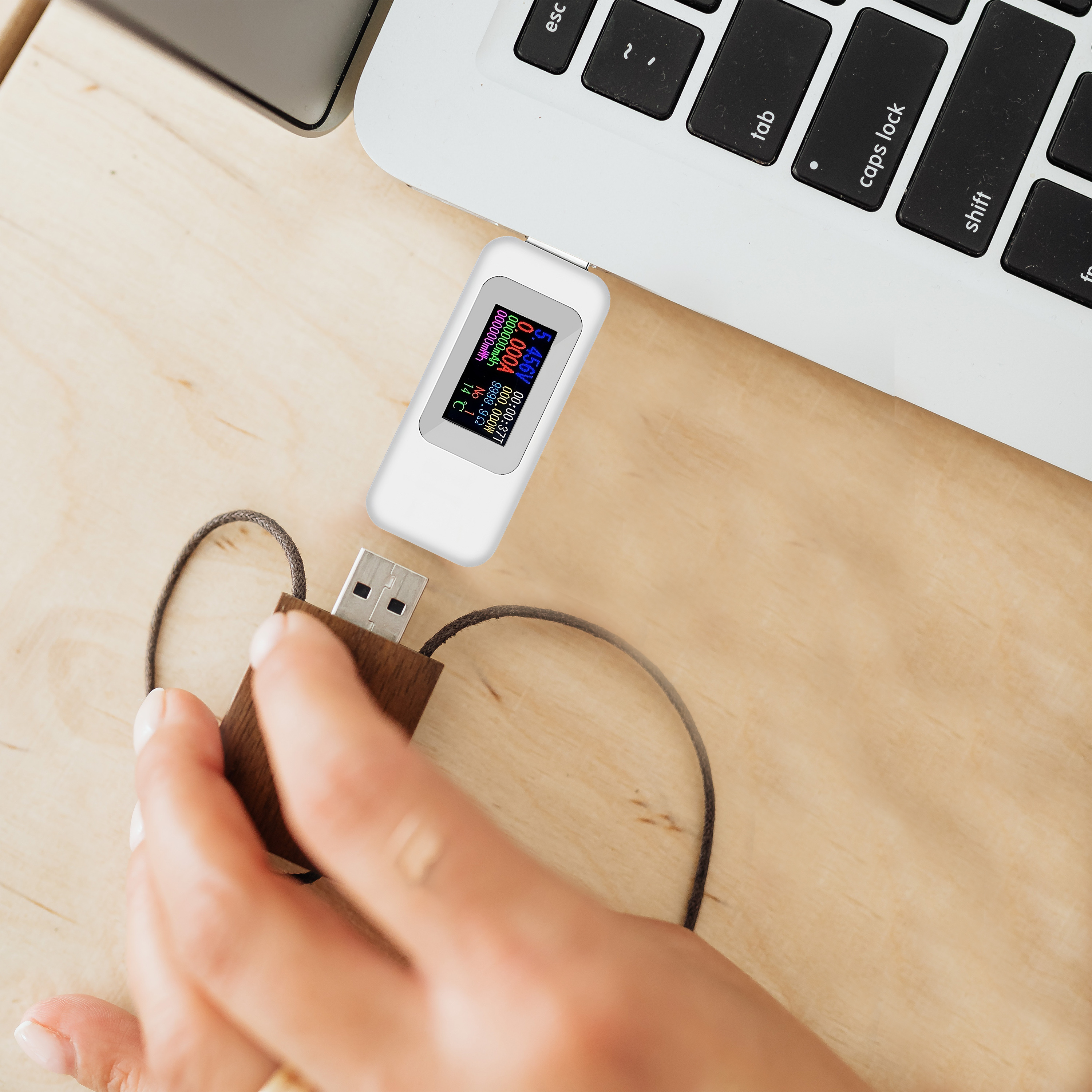 Eine Hand, die einen USB-Tester hält, der mit einem USB-Laufwerk und einem Laptop verbunden ist.