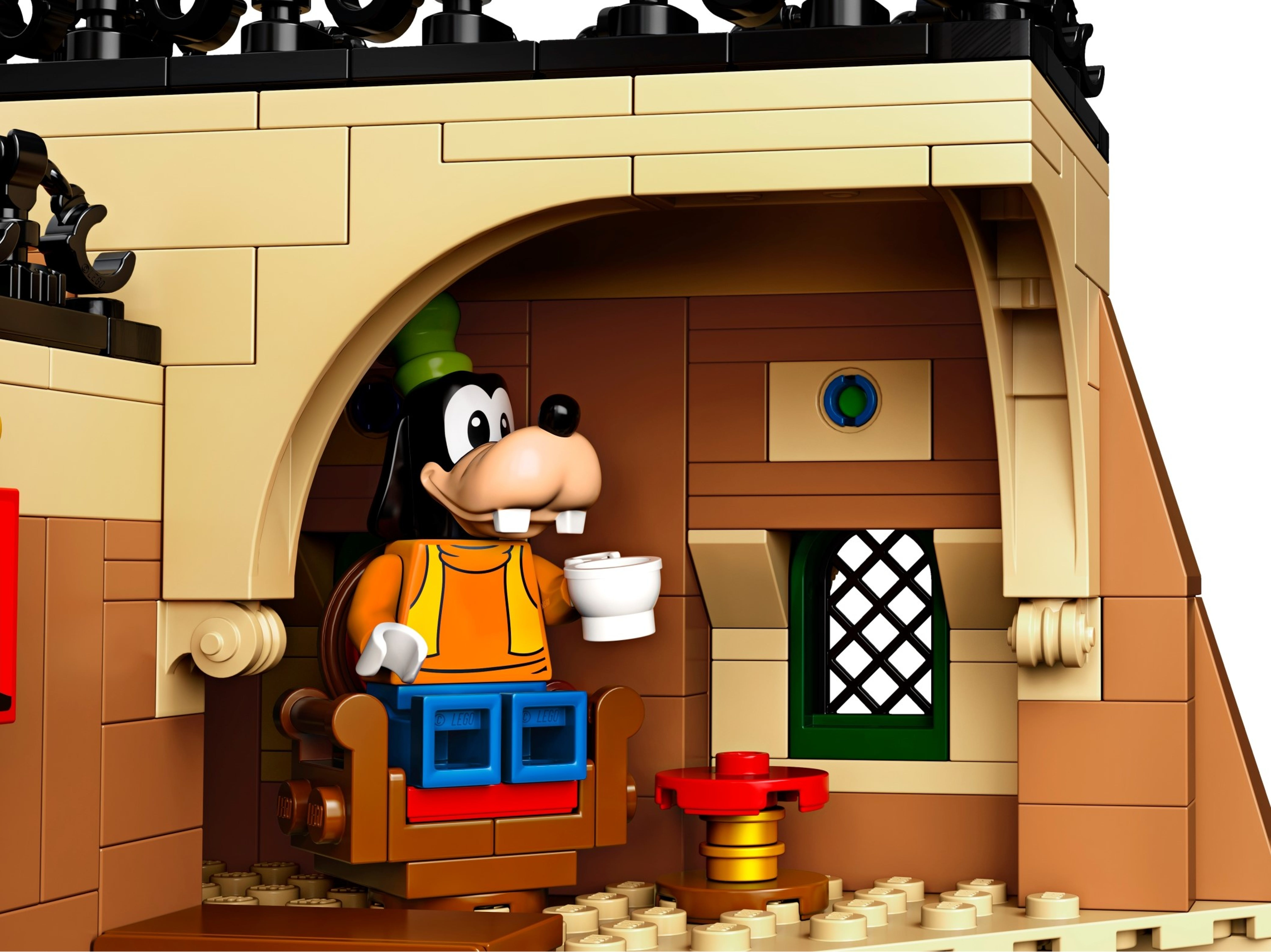 Figurka Lego Goofy siedząca w pokoju, trzymająca kubek. Wnętrze budynku.