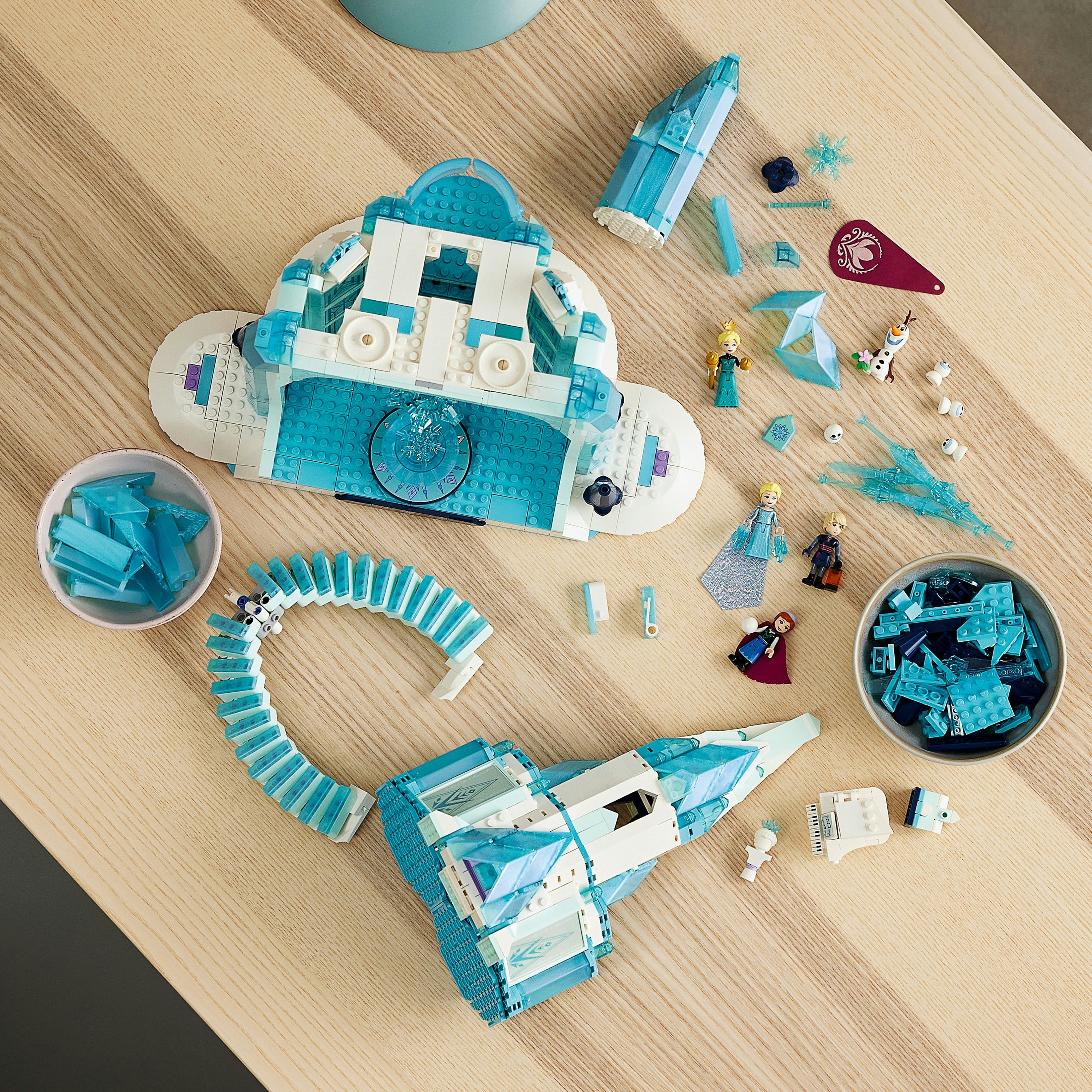 Zestaw Lego Frozen. Elementy lodowego zamku na drewnianym stole, z minifigurkami.