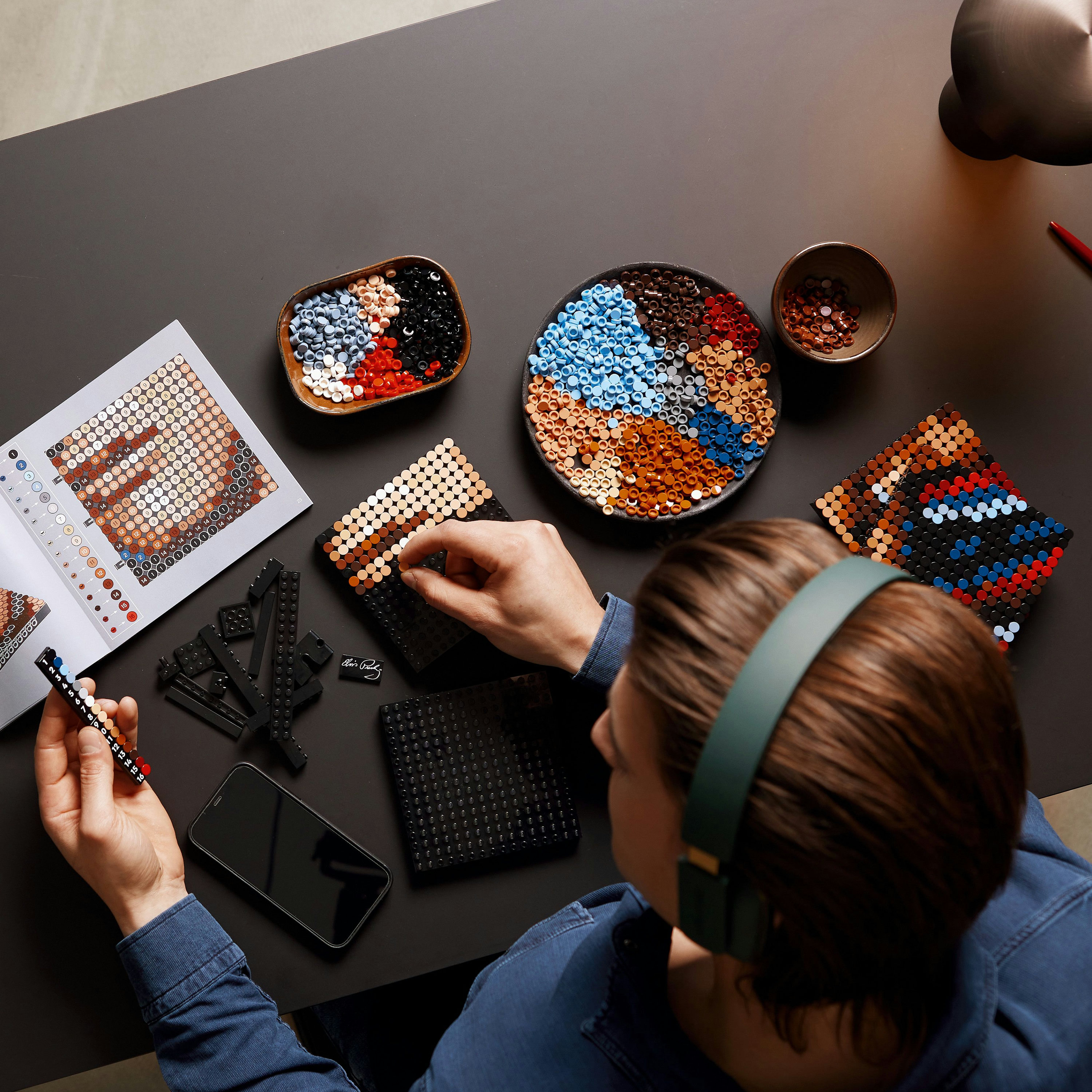 Osoba używająca Lego Dots na czarnym stole z akcesoriami i instrukcjami.