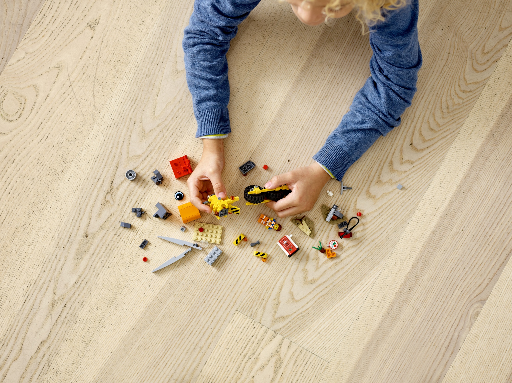 Un bambino gioca con i pezzi Lego su un pavimento di legno, costruendo un veicolo.