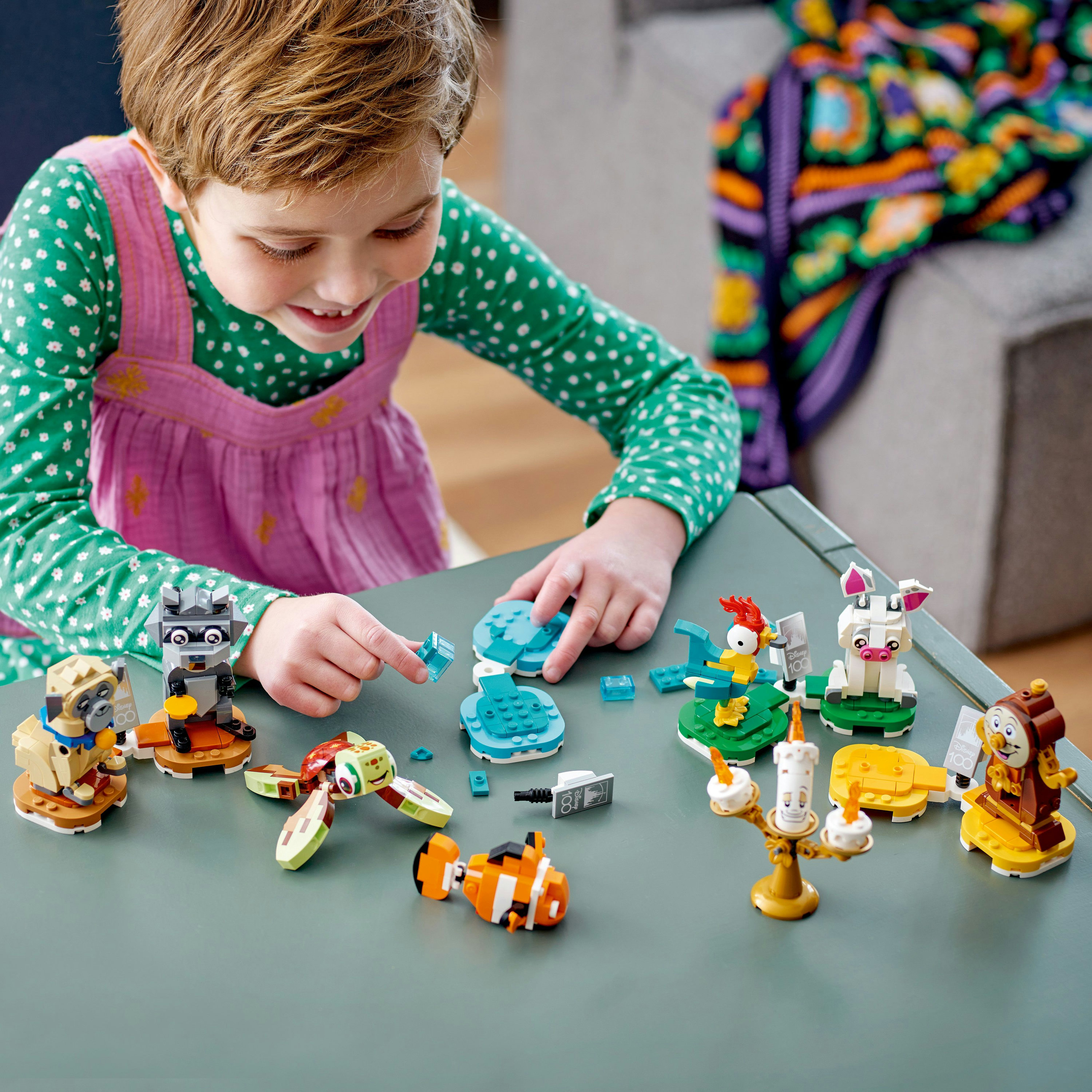 Yeşil bir masa üzerinde Lego figürleriyle oynayan bir çocuk. Çeşitli karakterler sergileniyor.