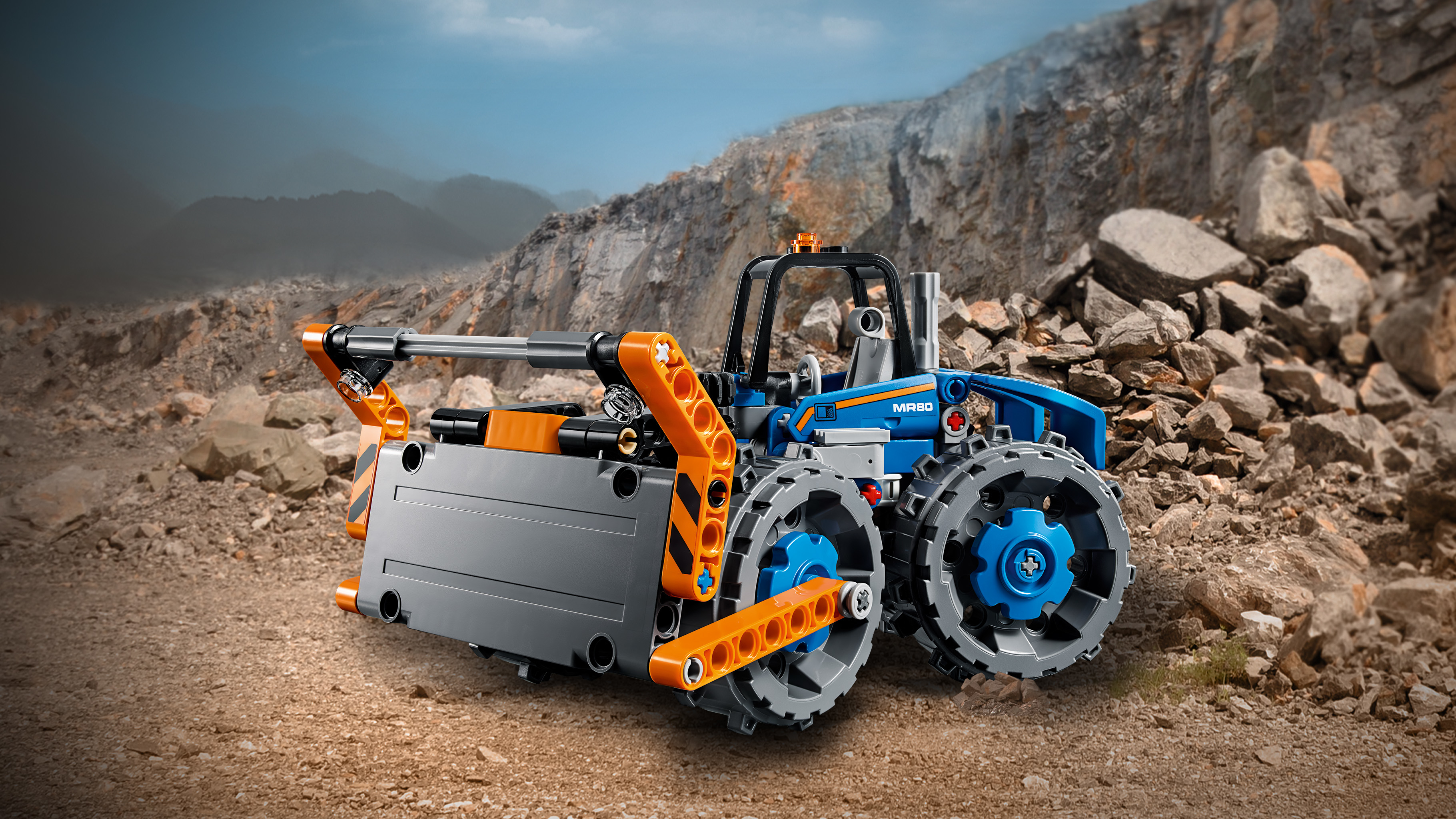 Zestaw Lego Technic spycharki. Spycharka jest niebiesko-pomarańczowa i znajduje się na powierzchni brązowej ziemi.