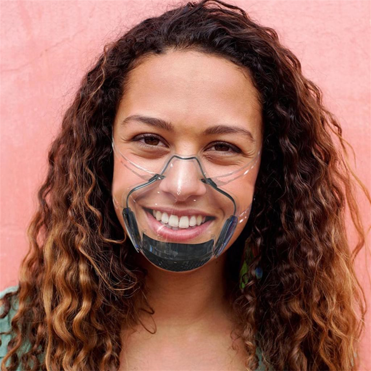 Eine Frau mit lockigem Haar trägt eine transparente Gesichtsmaske mit schwarzen Akzenten und lächelt.