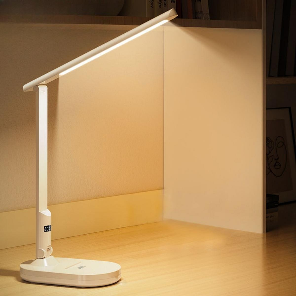 Eine weiße Schreibtischlampe steht auf einem Schreibtisch. Sie hat eine Digitalanzeige. Das Licht ist an.