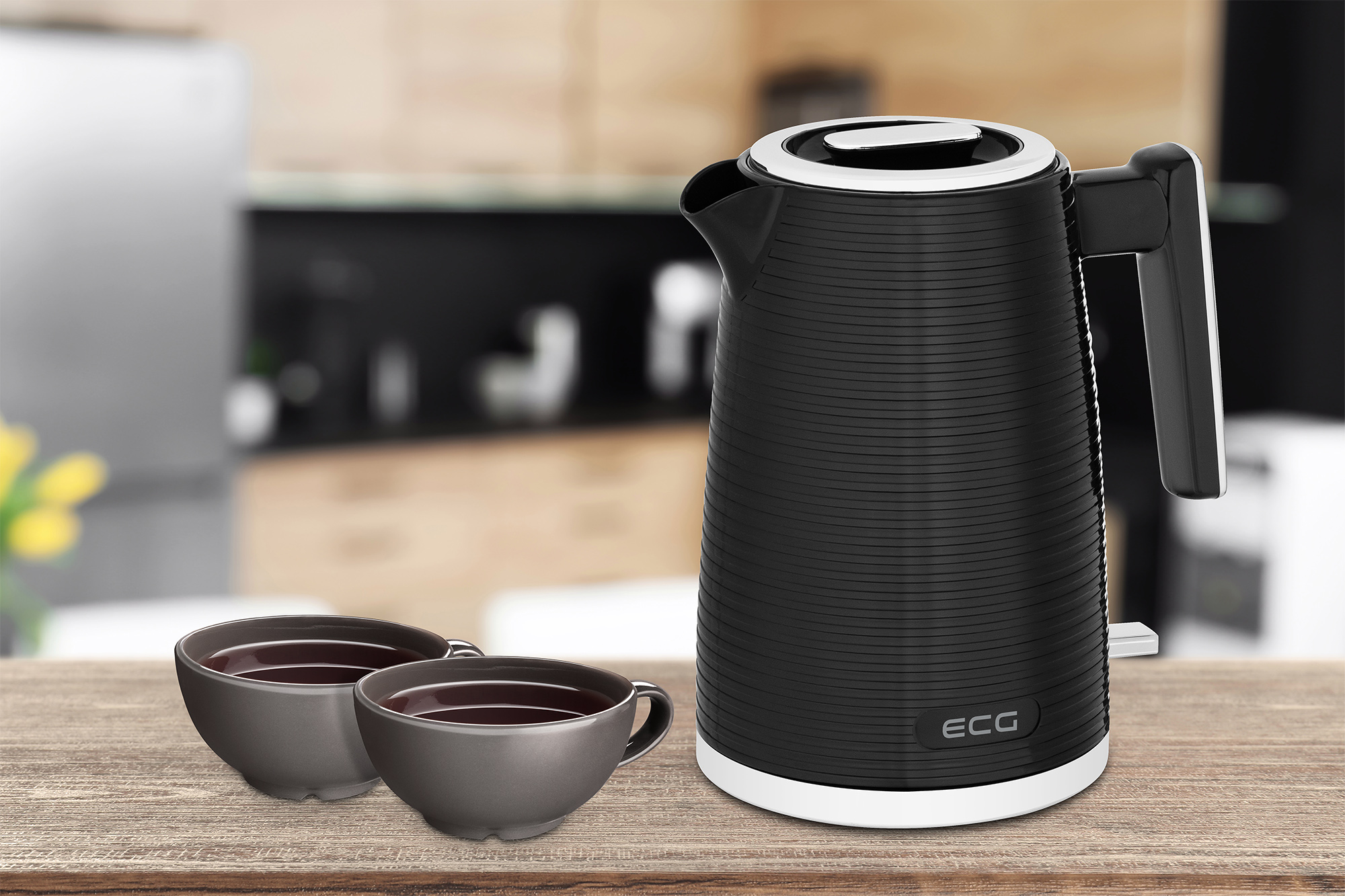 Czarny czajnik i dwie filiżanki na drewnianym stole. Rozmyte tło kuchni.