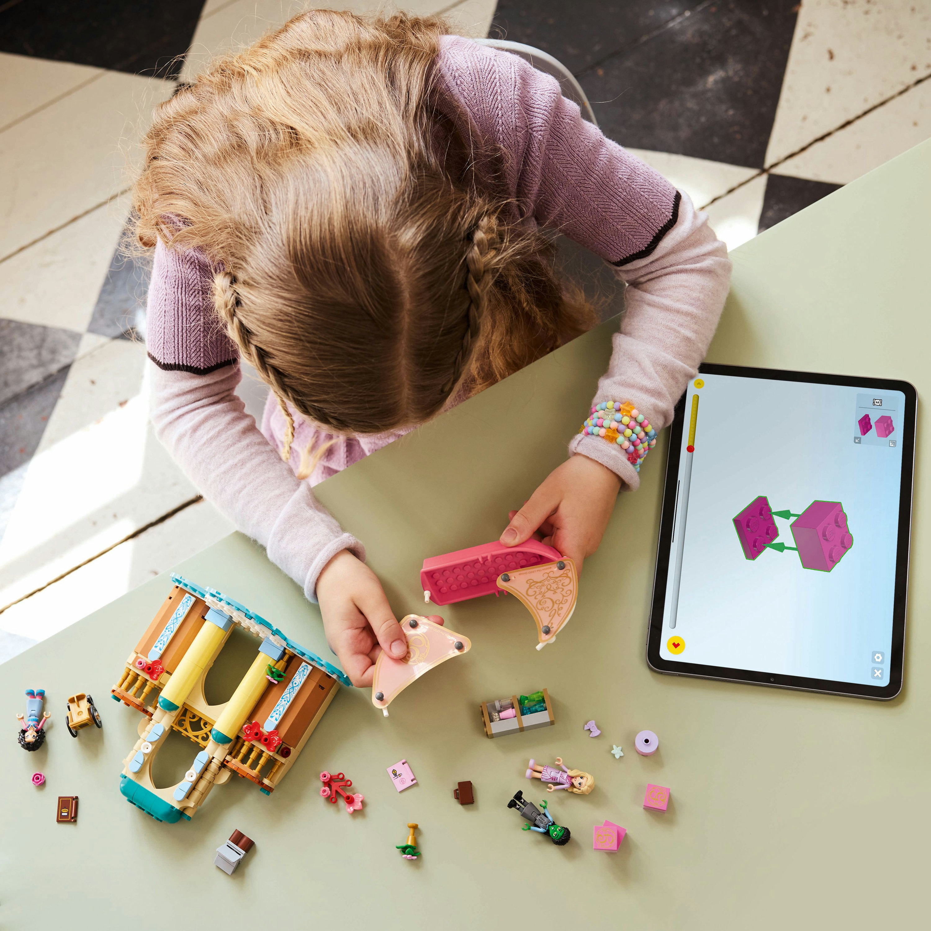 Dziecko buduje z Lego, korzystając z tabletu z instrukcjami, z rozrzuconymi różnymi elementami.