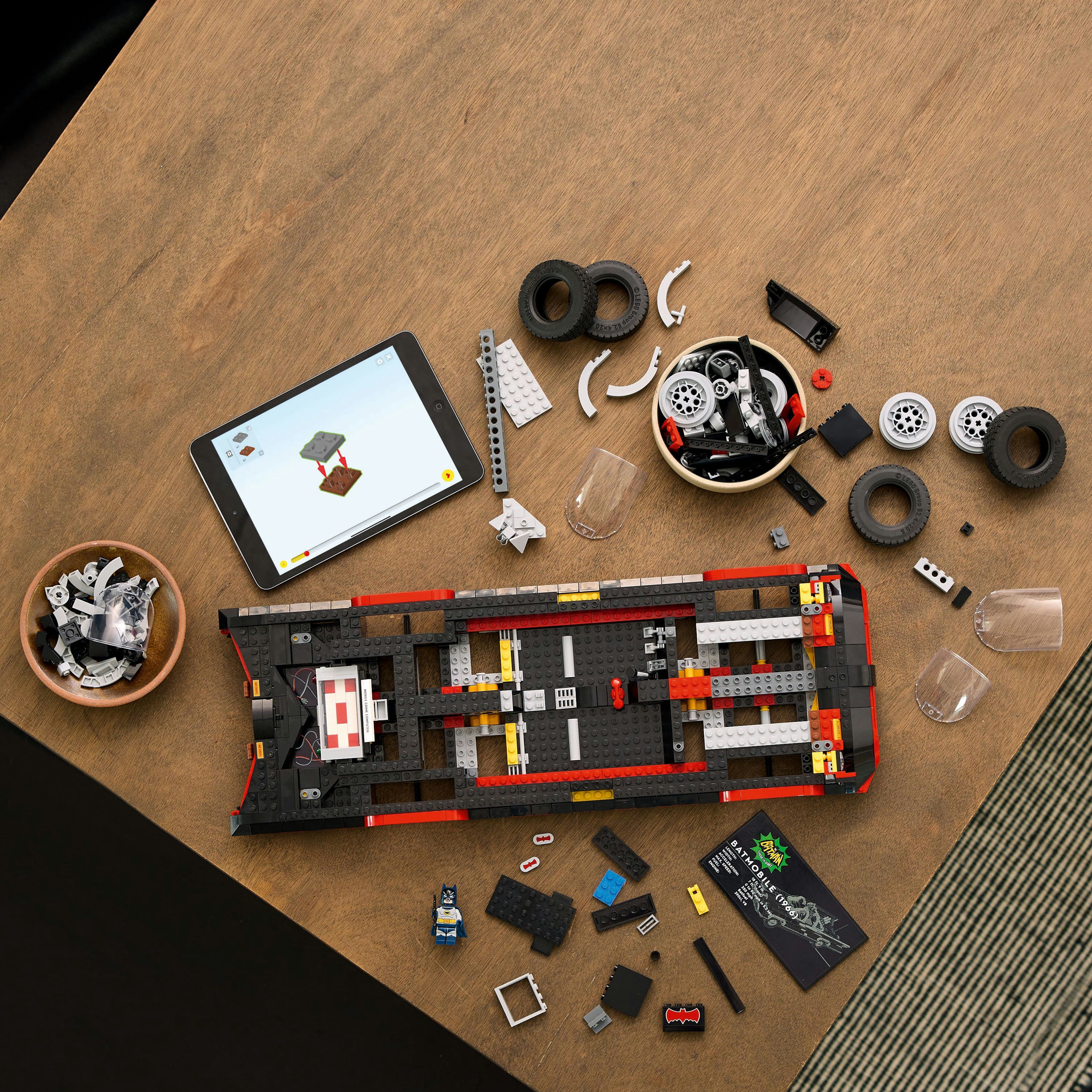 Costruzione Lego Batmobile. Parti e pezzi su un tavolo di legno con un tablet. Istruzioni visibili.