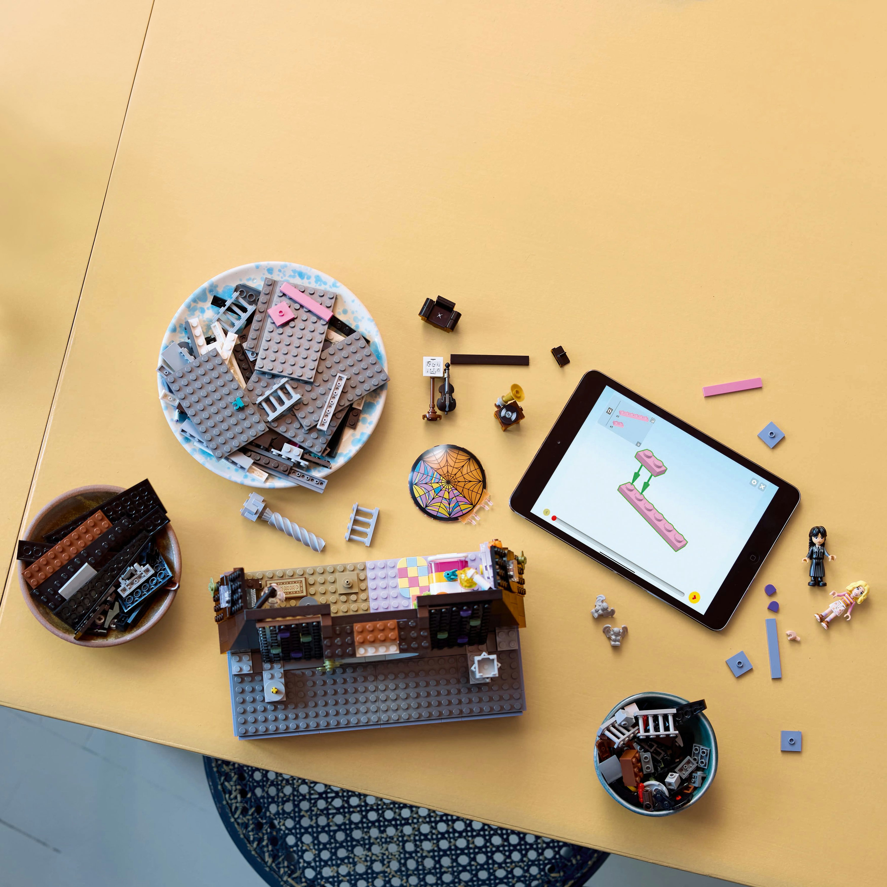 Budowa Lego na żółtym stole. Części w miskach, tablet pokazuje instrukcje.