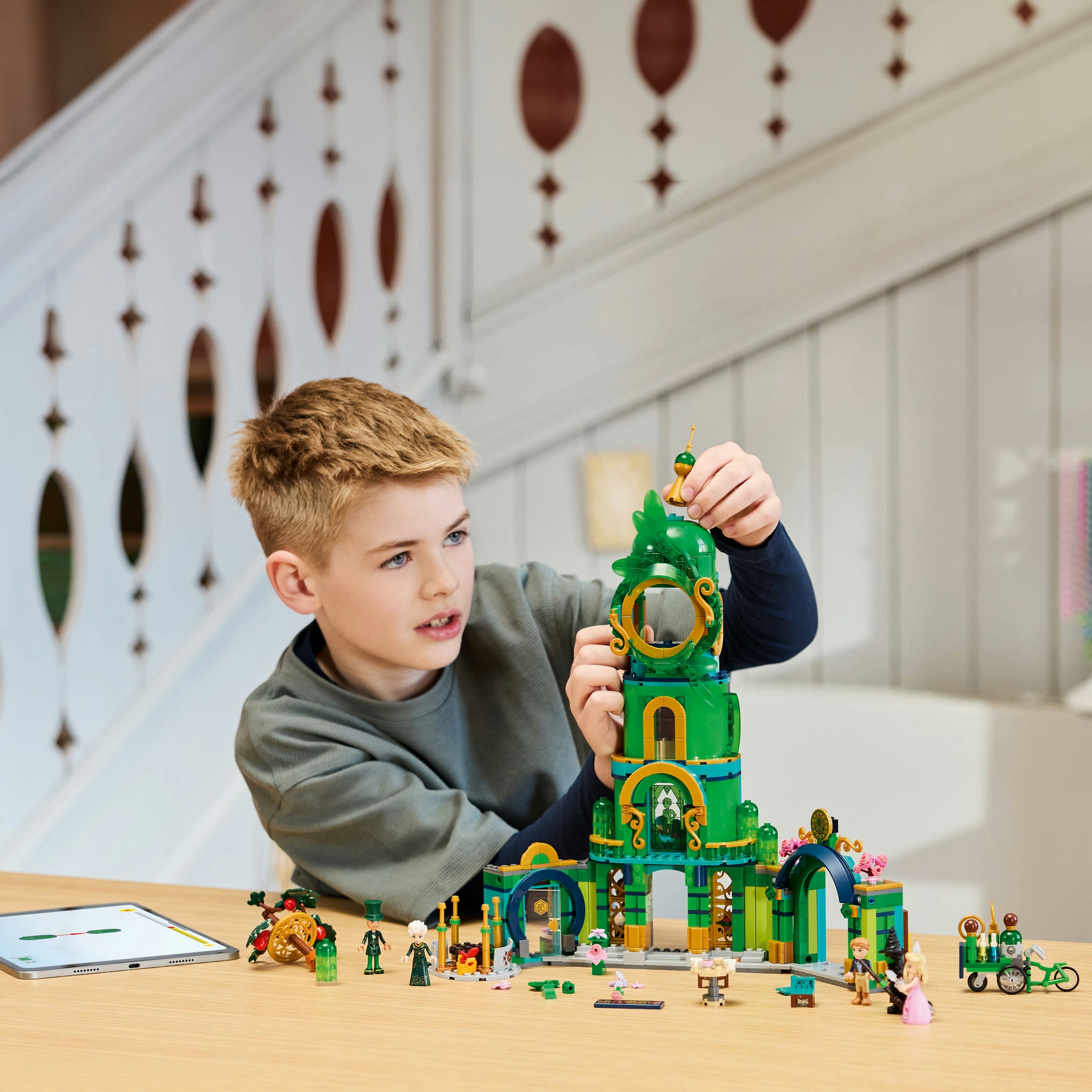 Un niño construye un juego de Lego con un edificio verde y dorado. Otras piezas de Lego en la mesa.