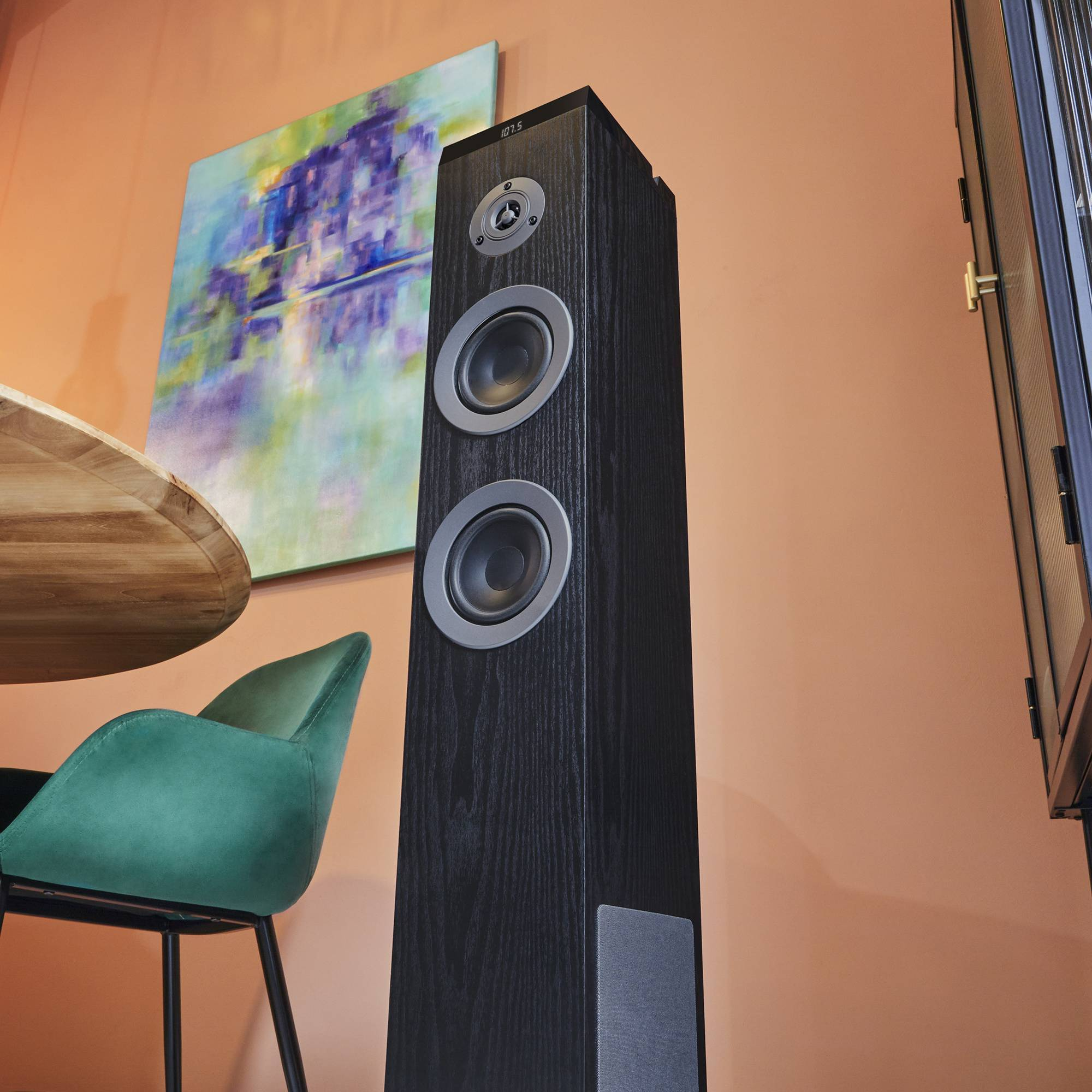 Un altavoz negro alto con dos altavoces, junto a una pintura y una mesa.