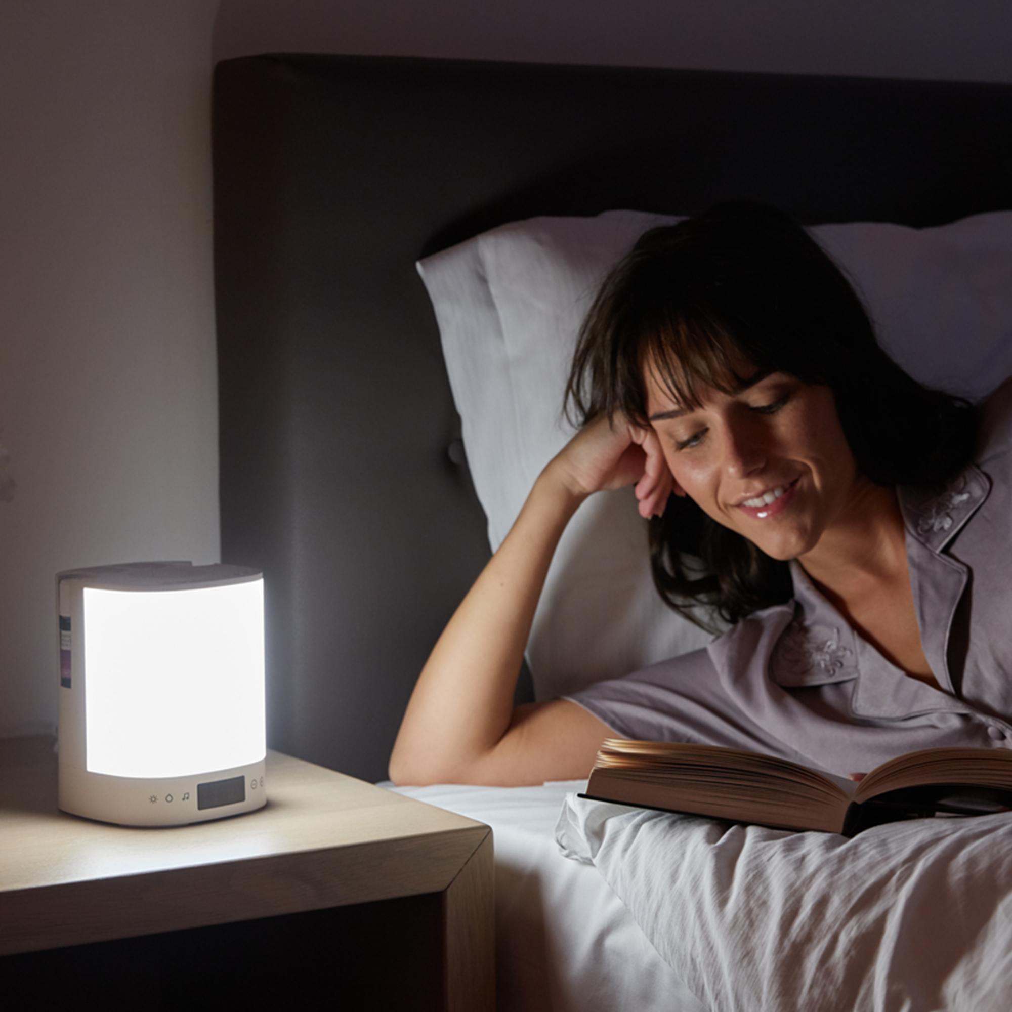 Woman in bed reading under a bright white lamp.