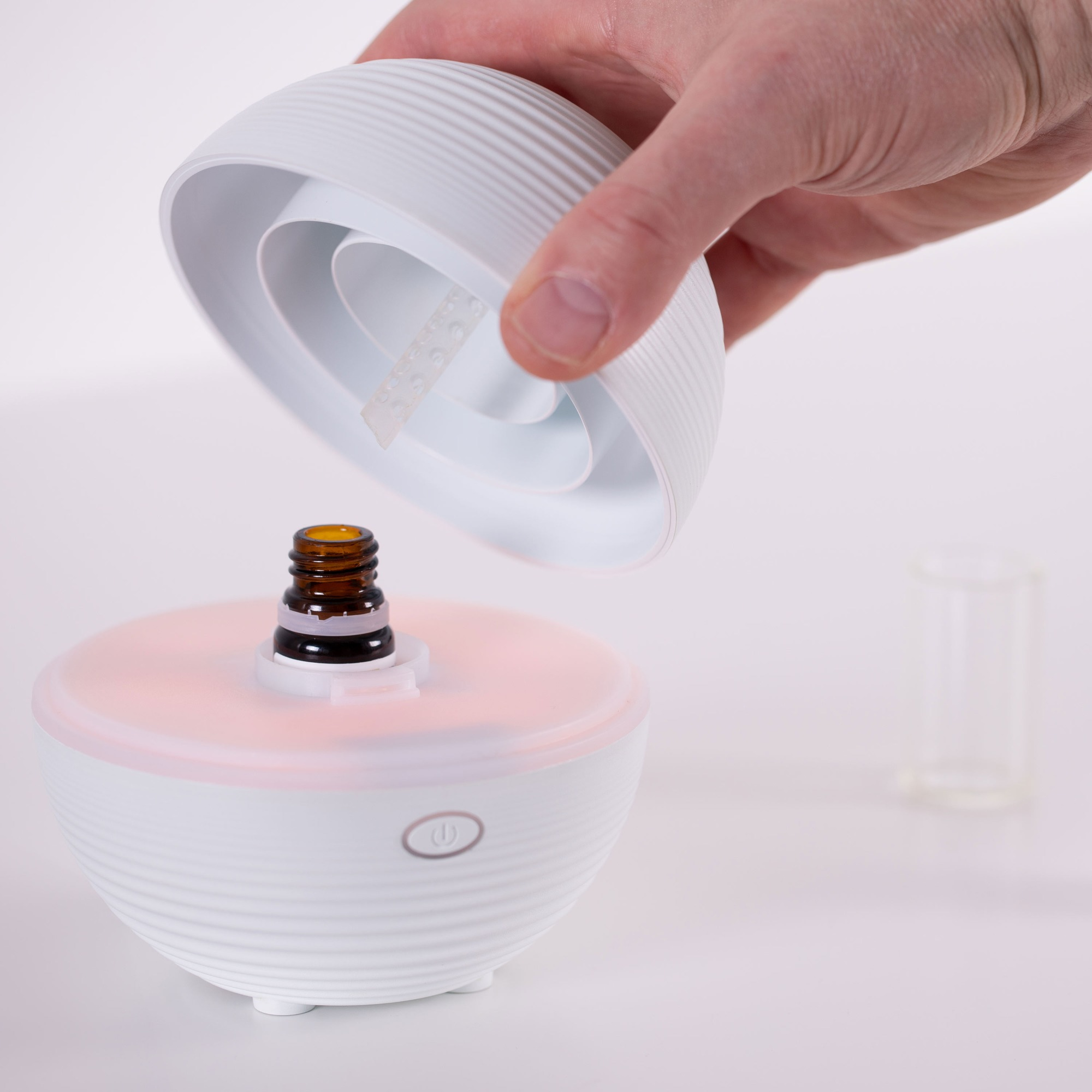 A white essential oil diffuser with a brown bottle being placed inside, on a white surface.