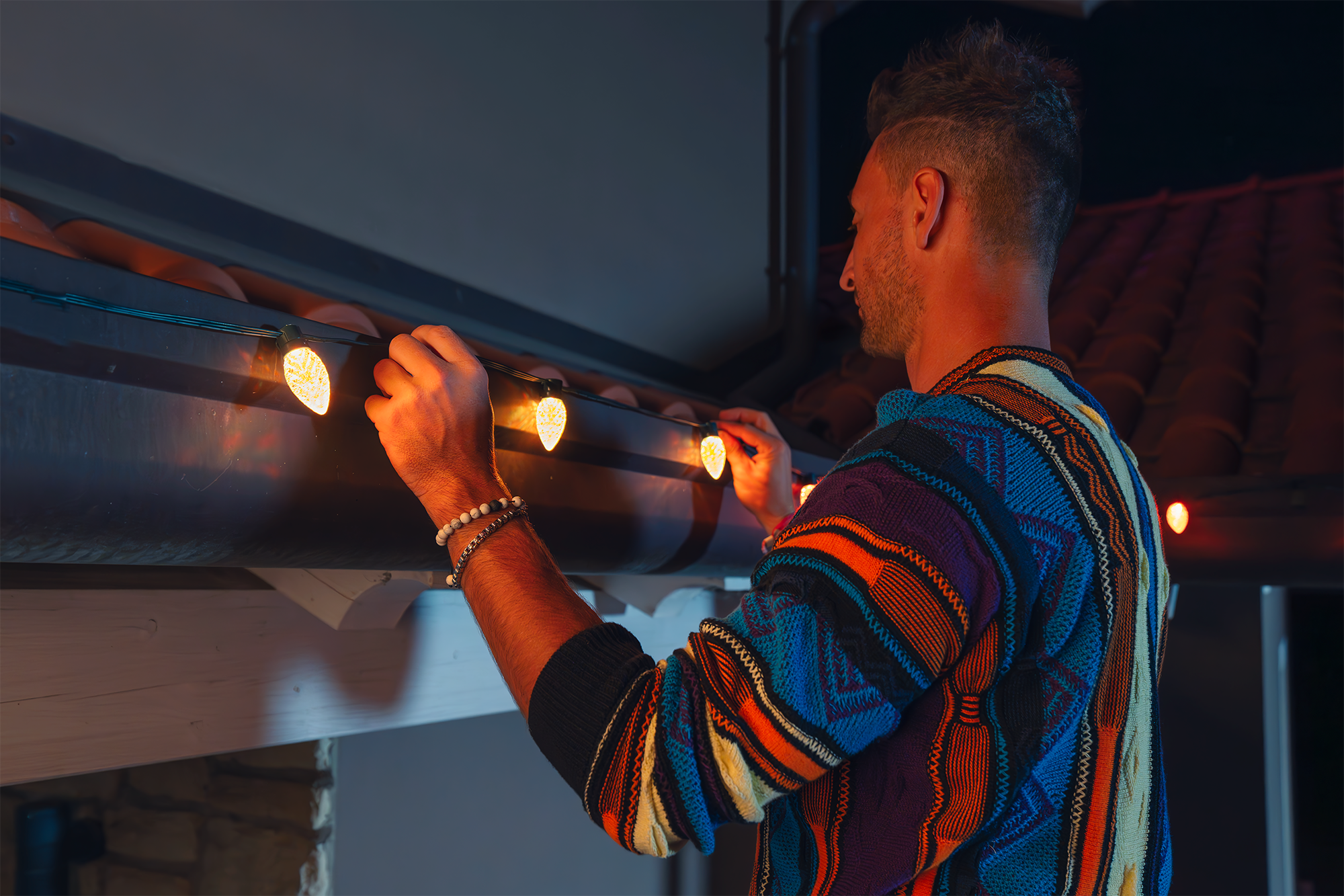 Uomo che installa luci a stringa su una casa. Le luci sono gialle e la casa è buia.