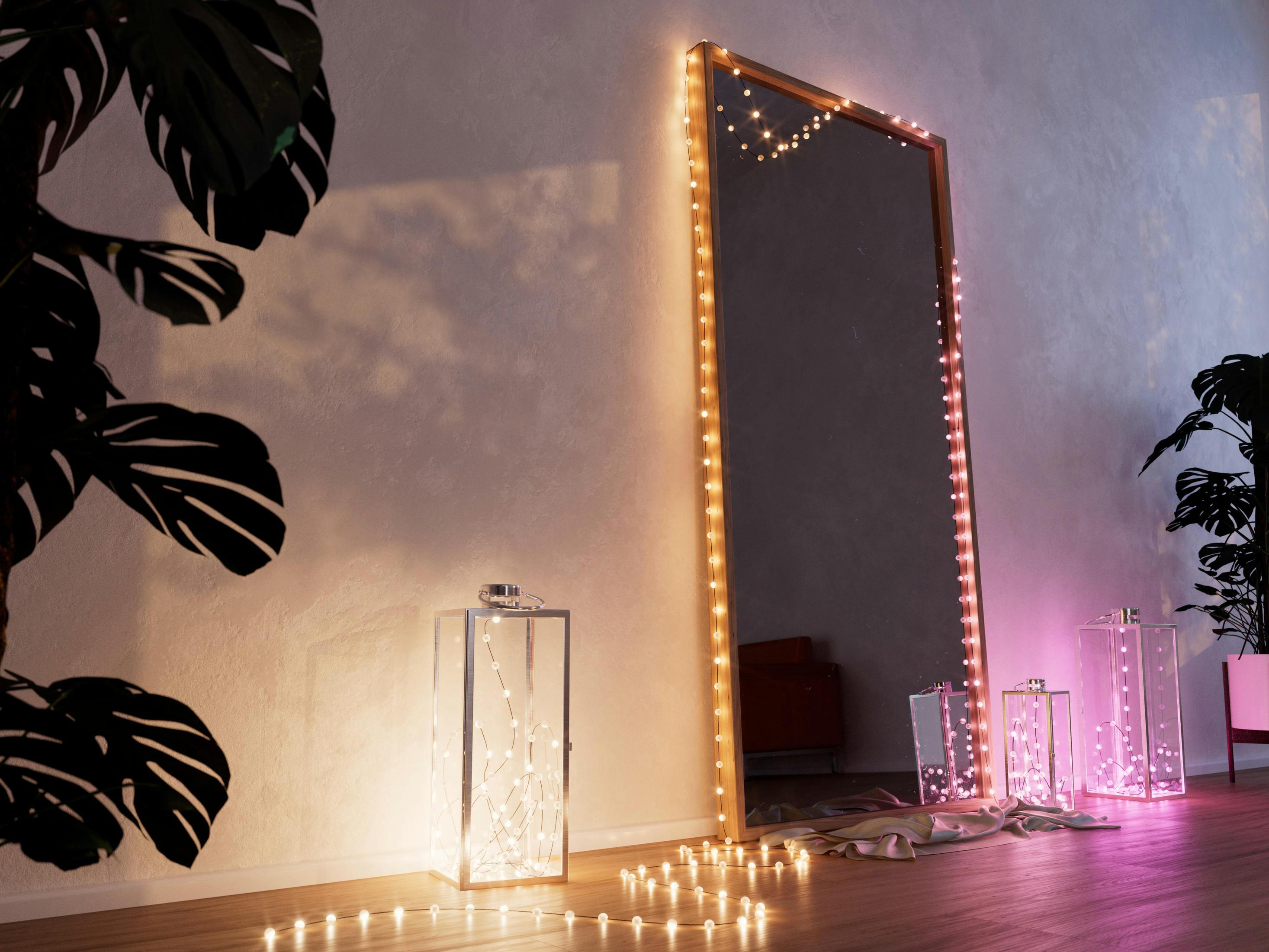 Duże lustro z oświetleniem, otoczone dekoracjami i roślinami, tworzące ciepłą atmosferę.