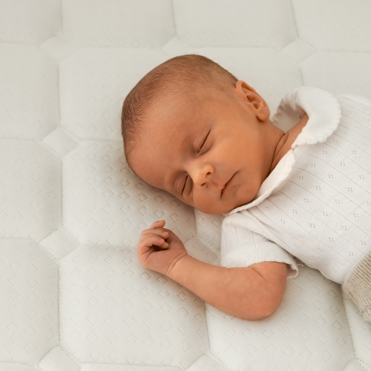 Bebé recién nacido durmiendo en un colchón blanco acolchado.