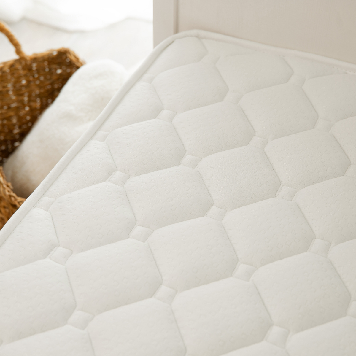 Colchón blanco con superficie texturizada. Una cesta y una almohada en el fondo.