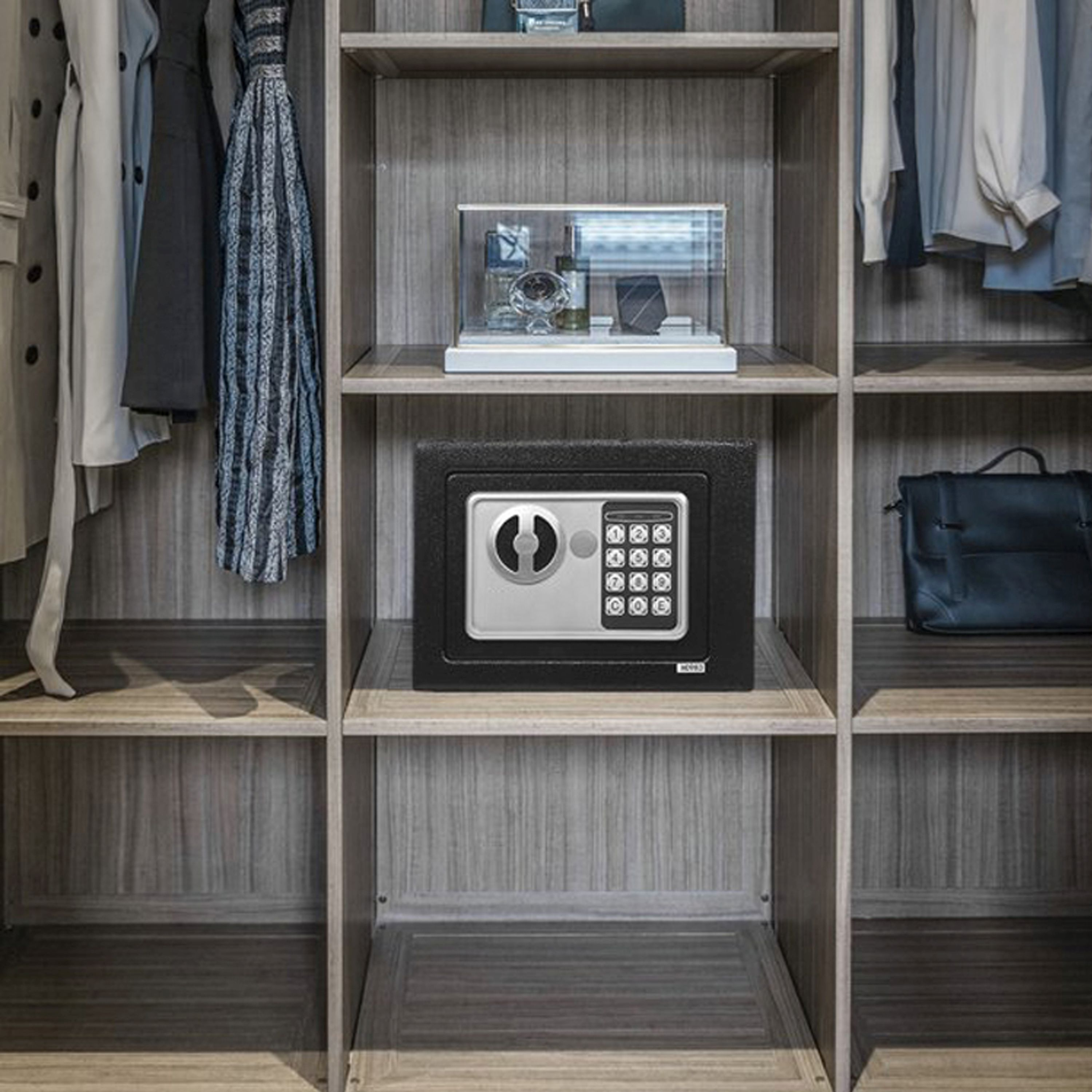 Ein schwarzer Safe mit digitalem Tastenfeld, der sich in einem Holzschrank befindet, mit Kleidung herum.
