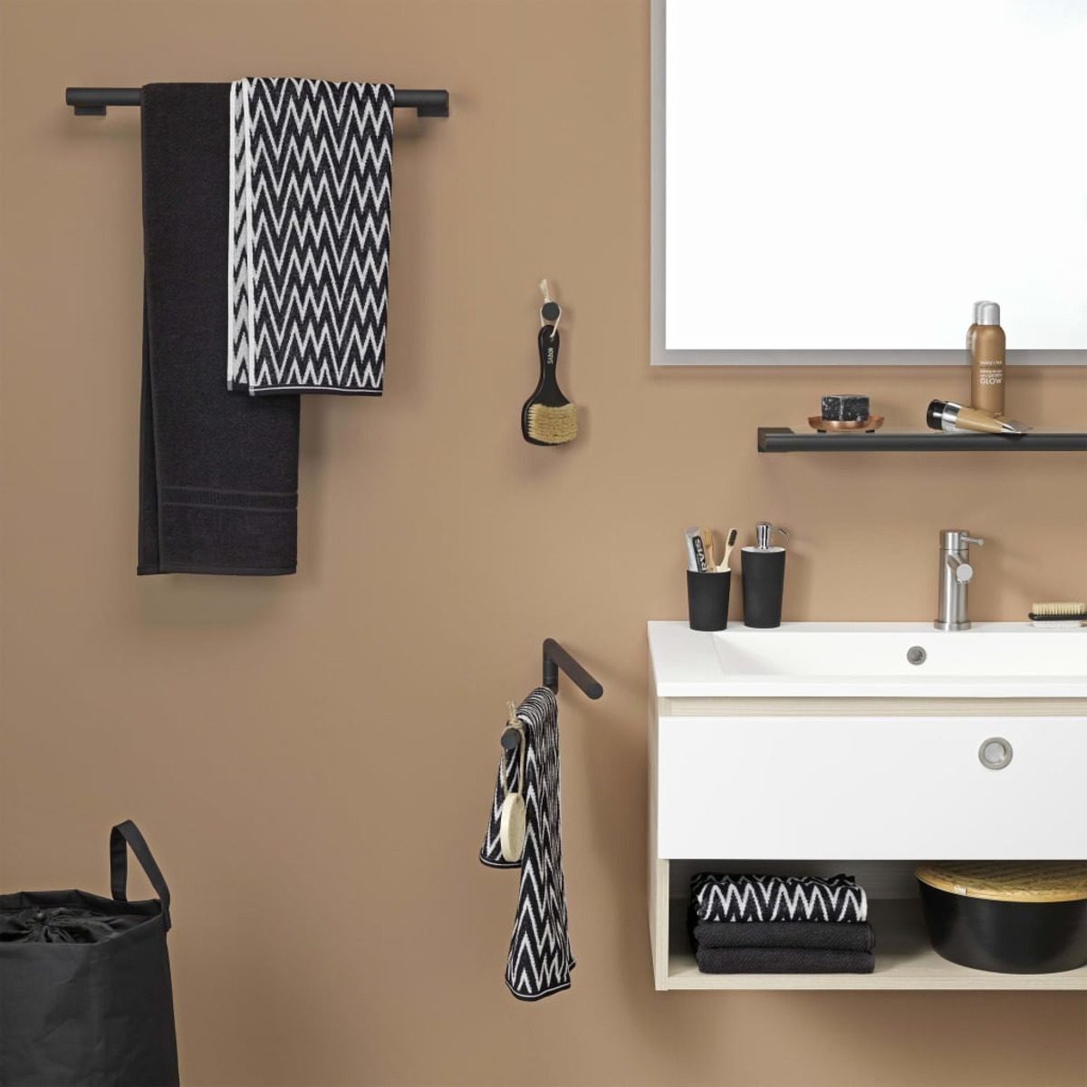 Badezimmer mit schwarzen Handtüchern, Spiegel und Waschbecken. Beige Wand, schwarze Akzente.