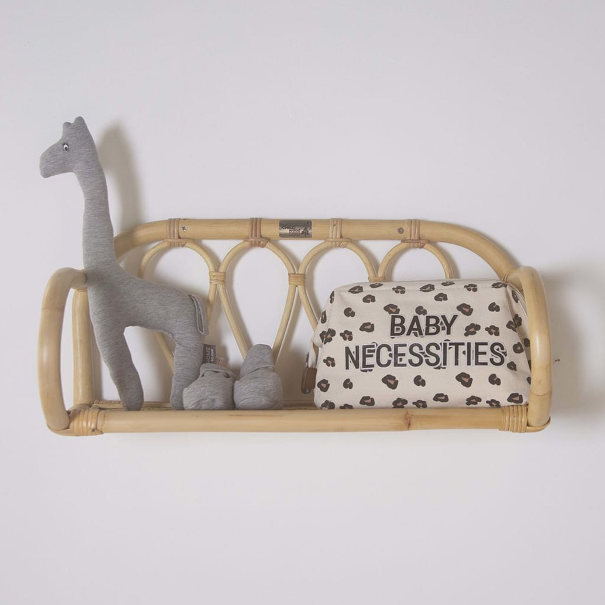Ein Rattans Regal mit einer Giraffe, zwei kleinen grauen Objekten und einer Baby-Utensilientasche.