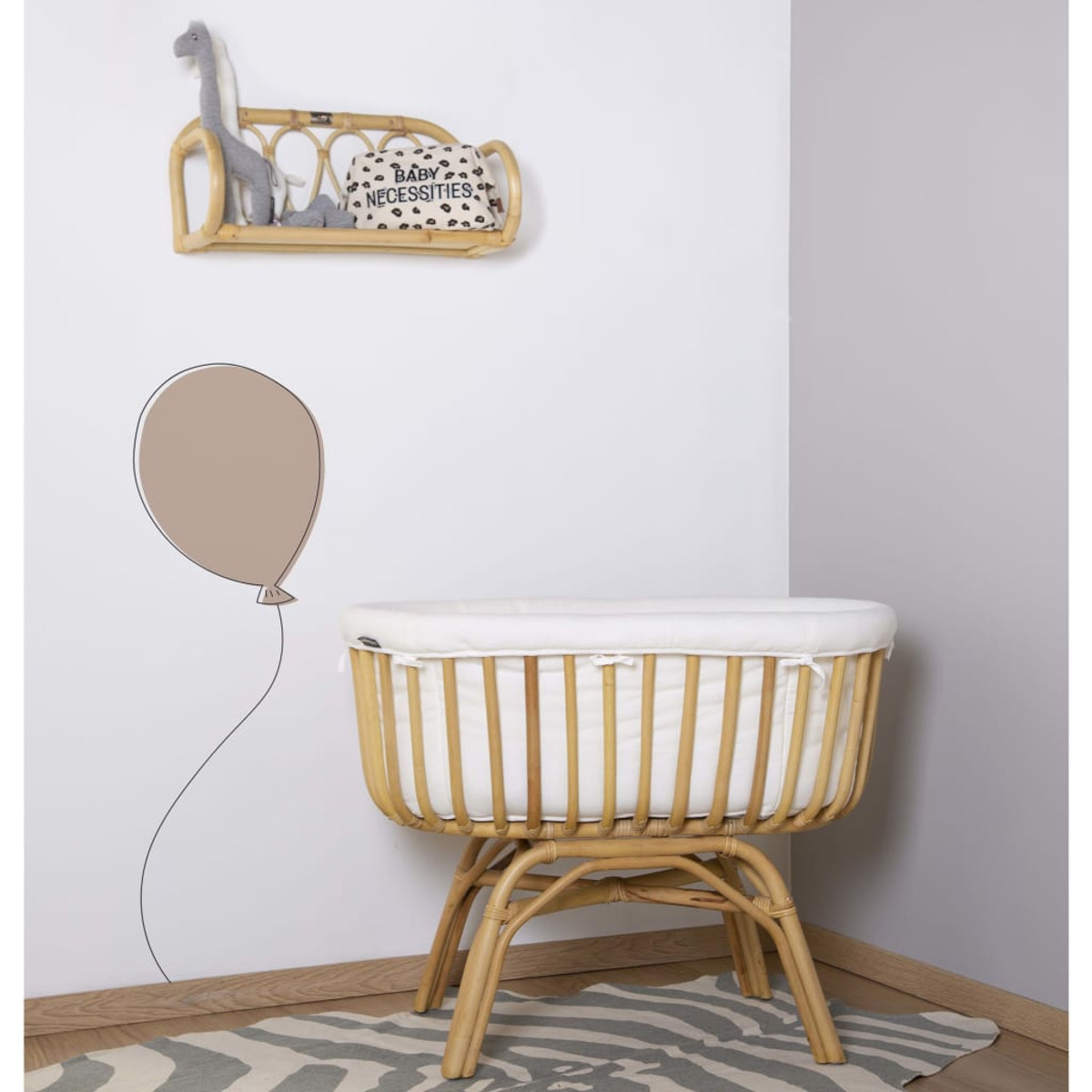 Ein Babybett aus gewebtem Holz, mit weißer Matratze, vor einer weißen Wand, mit einem Regal und einem Zebra-Teppich.