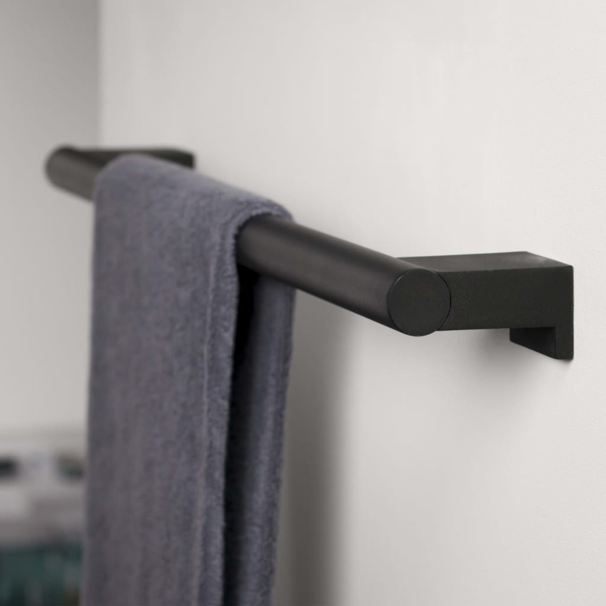 Schwarzer Handtuchhalter mit grauem Handtuch an einer weißen Wand.