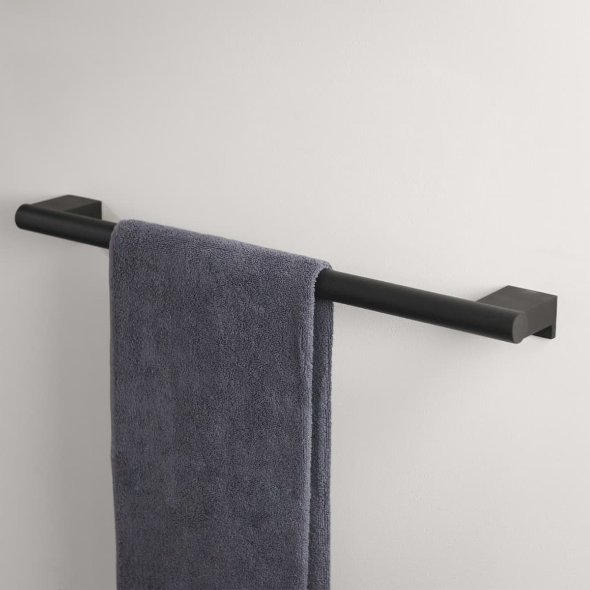 Schwarzer Handtuchhalter mit einem grauen Handtuch. Die Stange ist an einer weißen Wand befestigt.