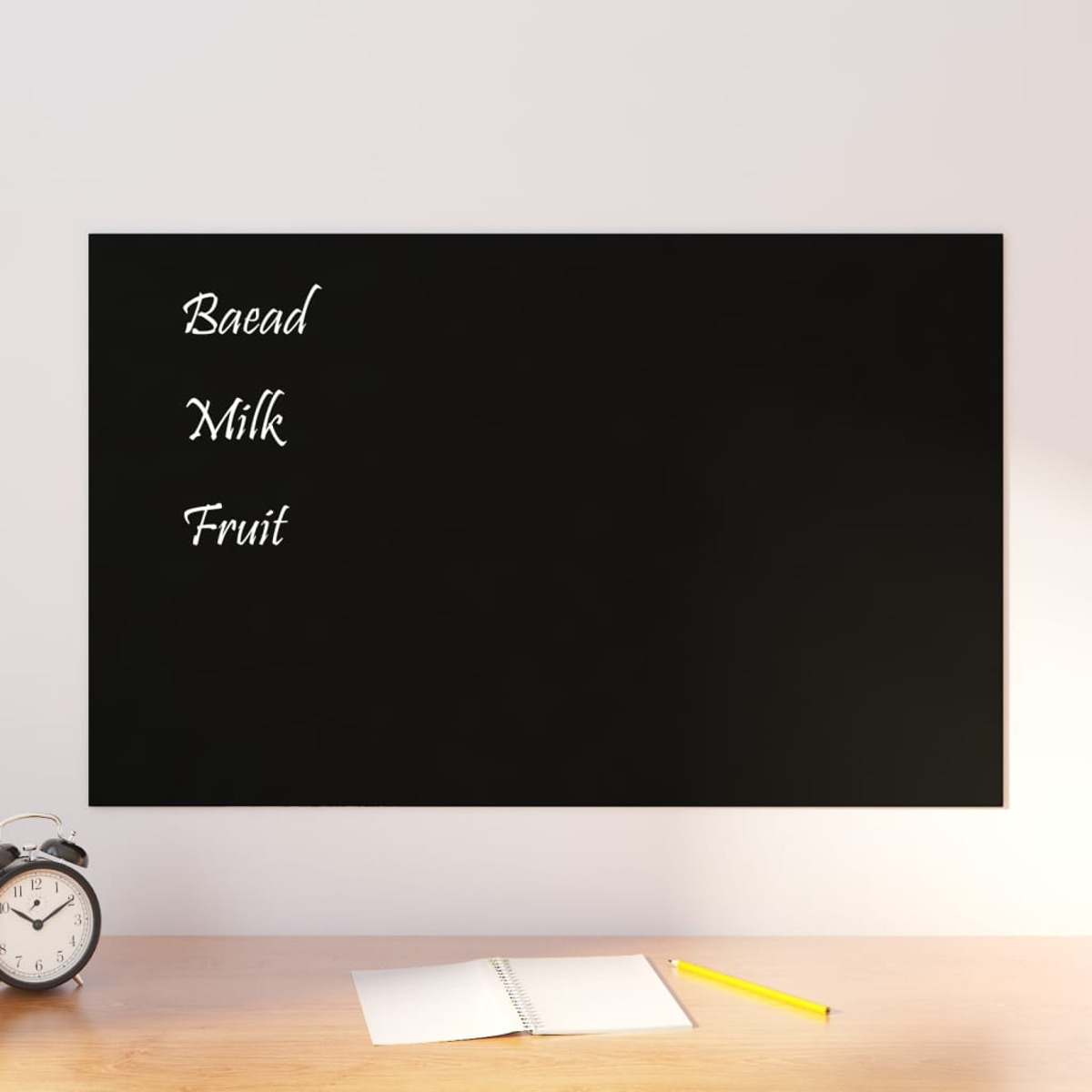 Schwarze Tafel mit den Worten "Brot, Milch, Obst". Ein Wecker und ein Notizblock in der Nähe.