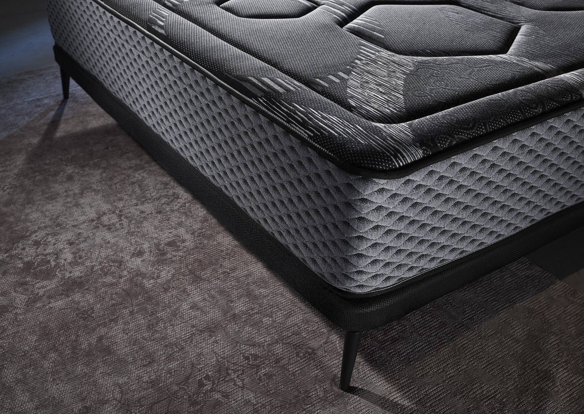 Primer plano de un colchón gris y negro con un patrón de diamantes, sobre una alfombra.