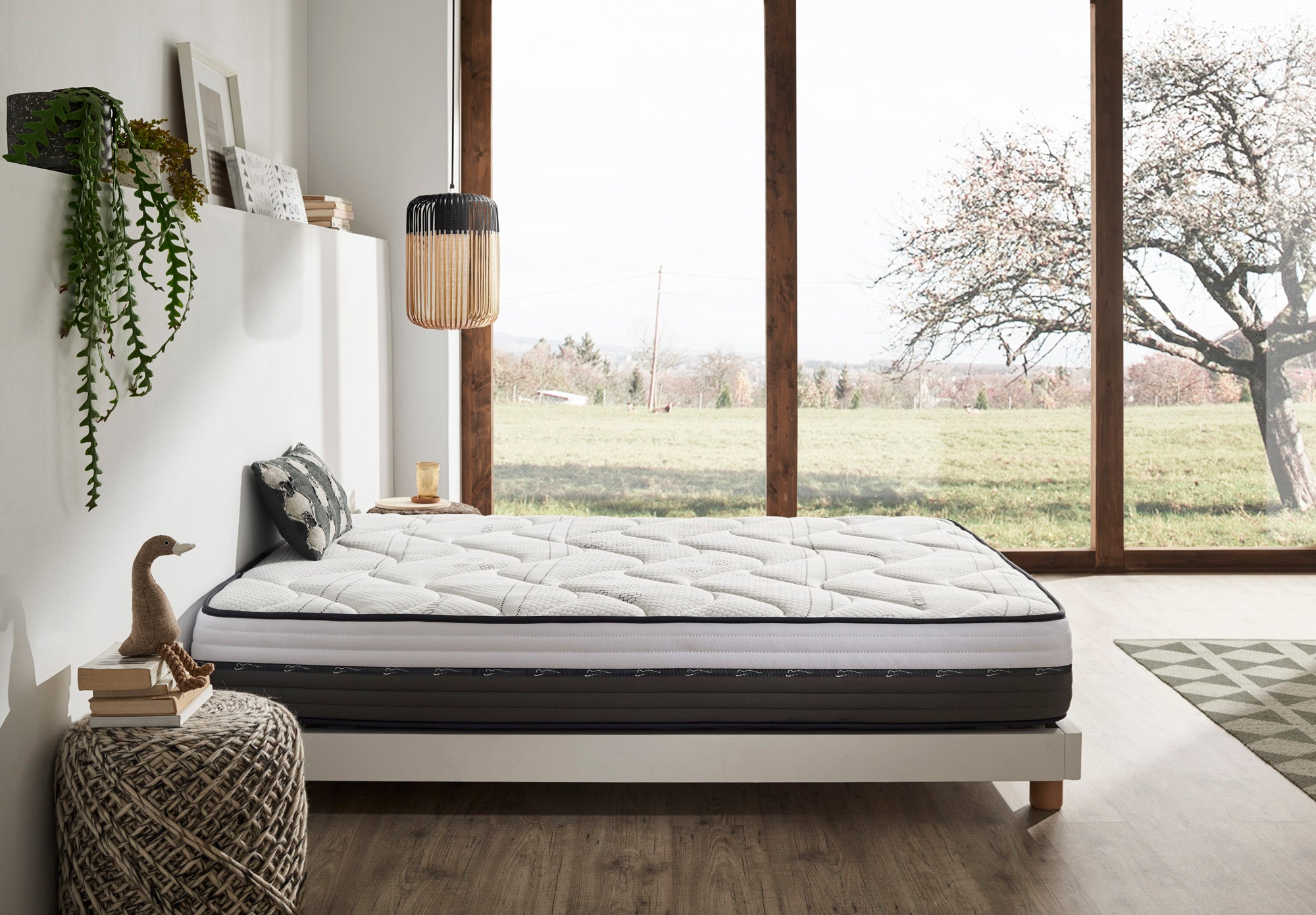 Dormitorio con cama, ventana grande y vista a campos verdes y un árbol.