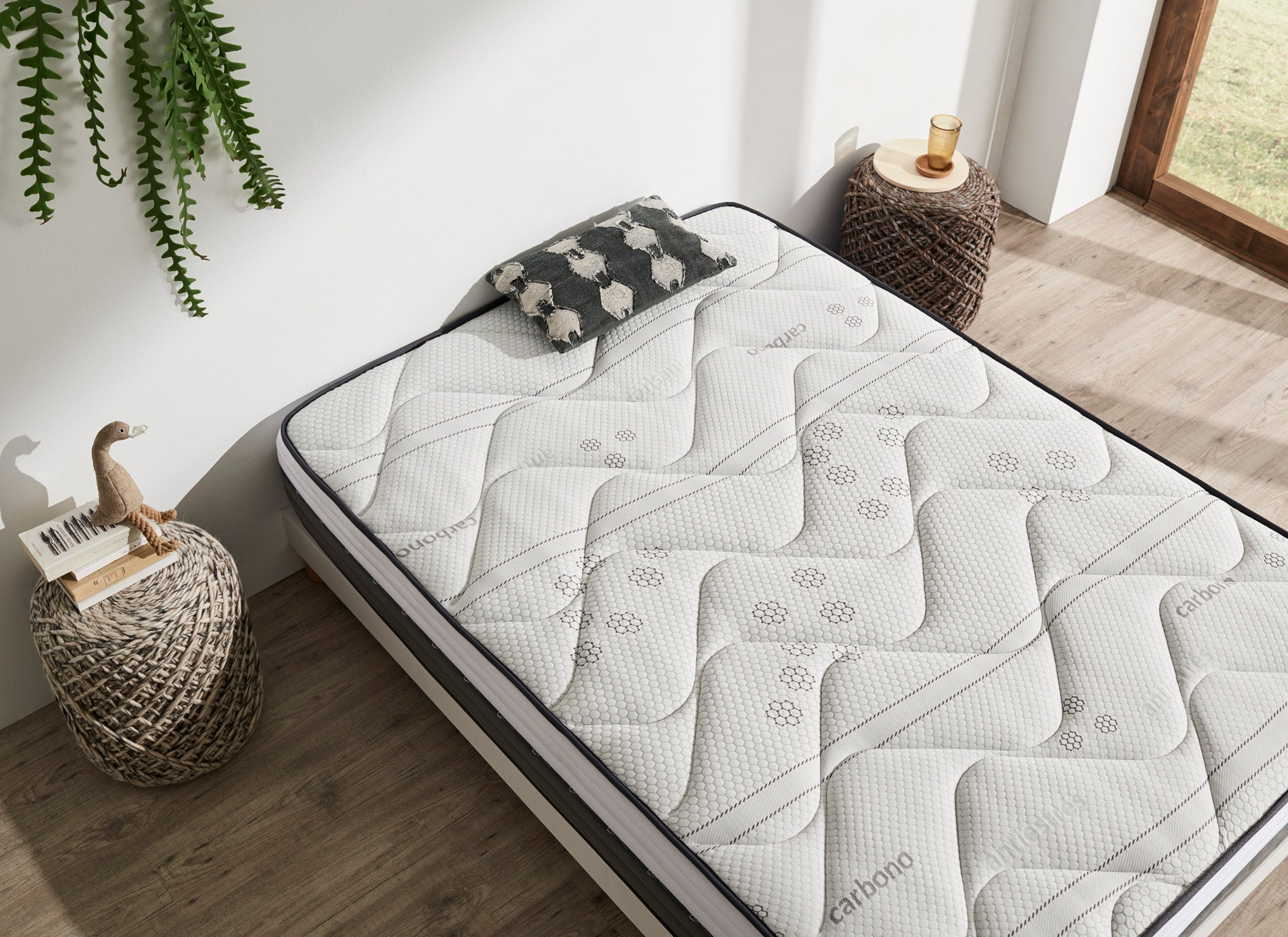 Colchón de cama doble con parte superior estampada gris, una almohada con estampado de oveja y una mesita de noche.