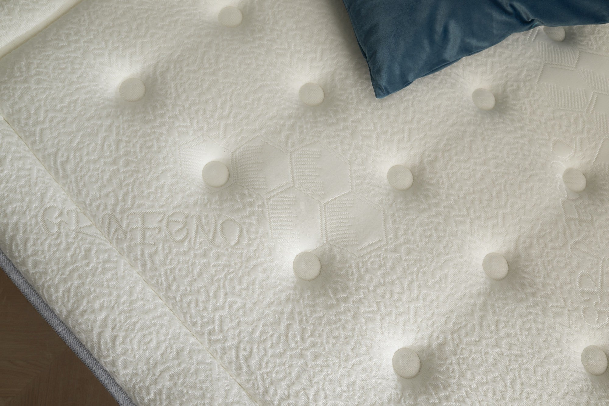 Primer plano de un colchón blanco con botones, una almohada azul arriba a la derecha.