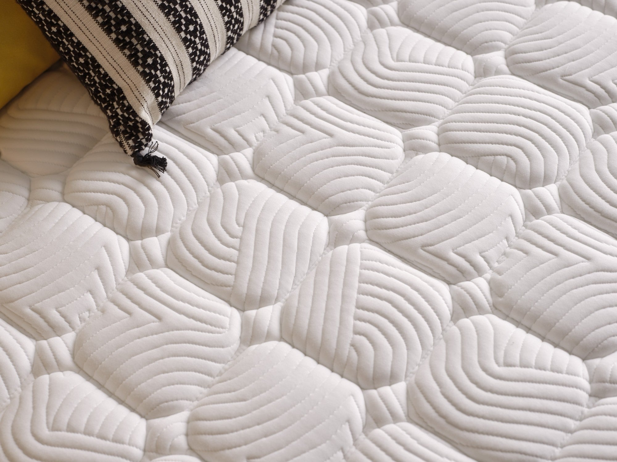 Primer plano de un colchón blanco acolchado con una almohada estampada en blanco y negro.