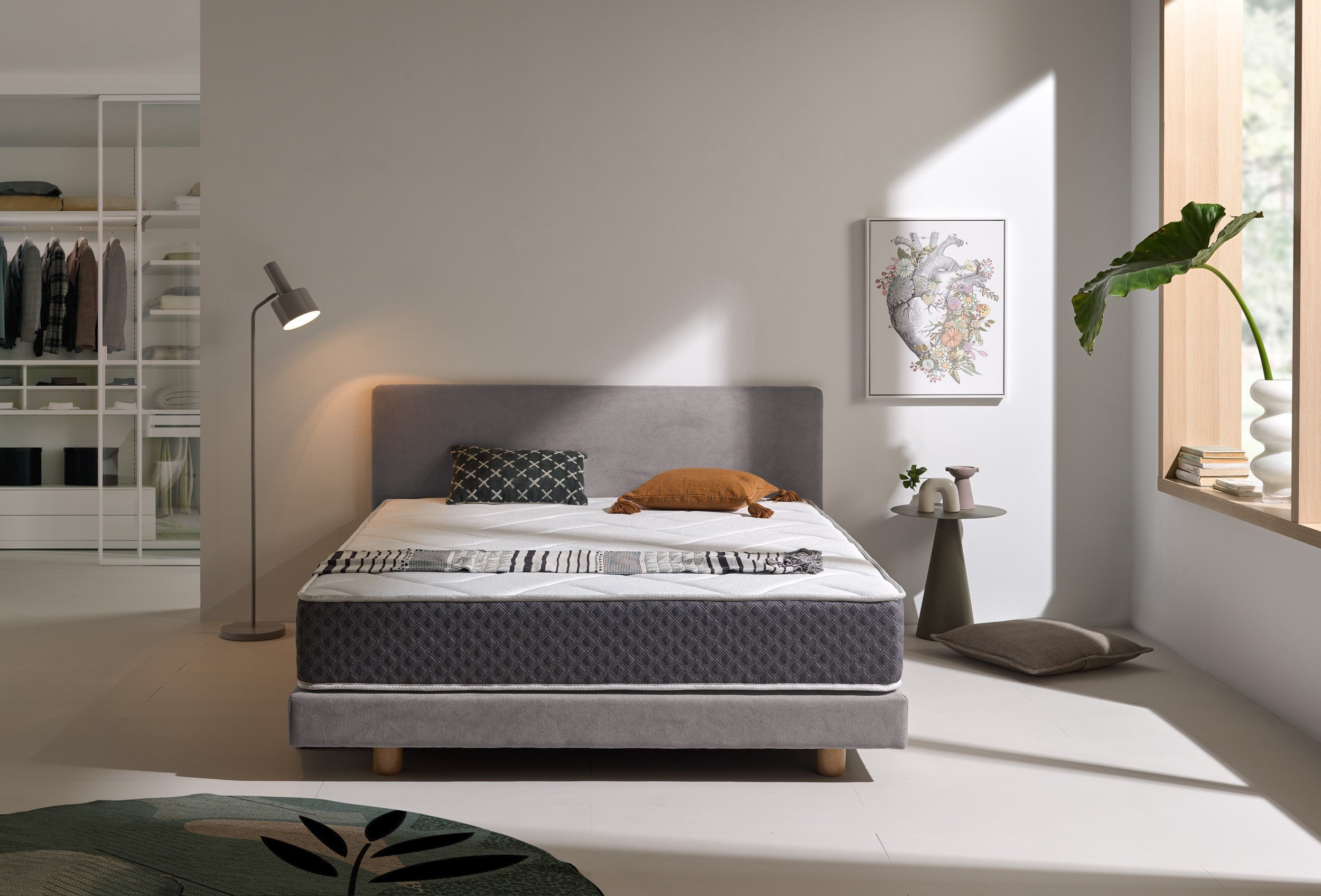 Un dormitorio con un colchón en un marco de cama, almohadas, arte y una lámpara.