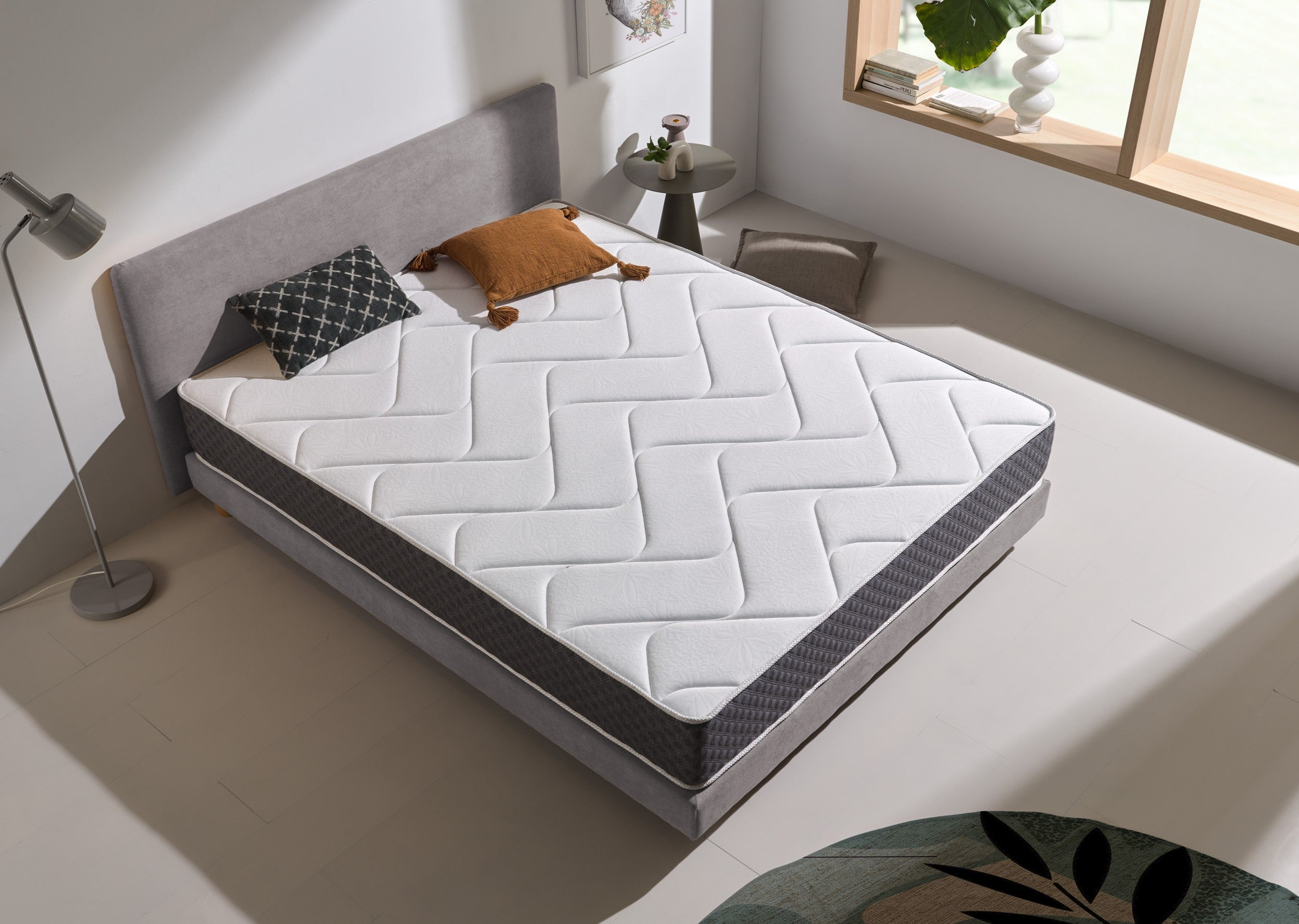 Cama con colchón estampado, almohada y ambiente moderno en tonos grises claros.