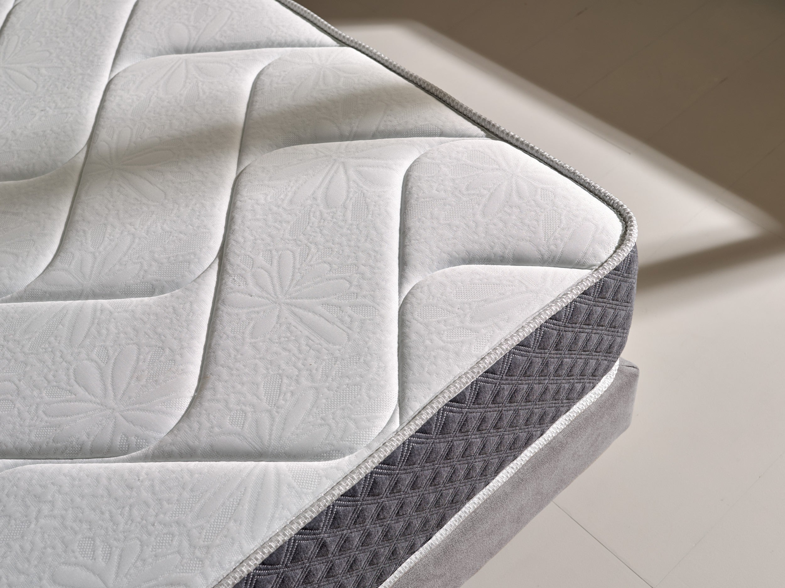 Primer plano de un colchón blanco con patrón floral y borde gris.