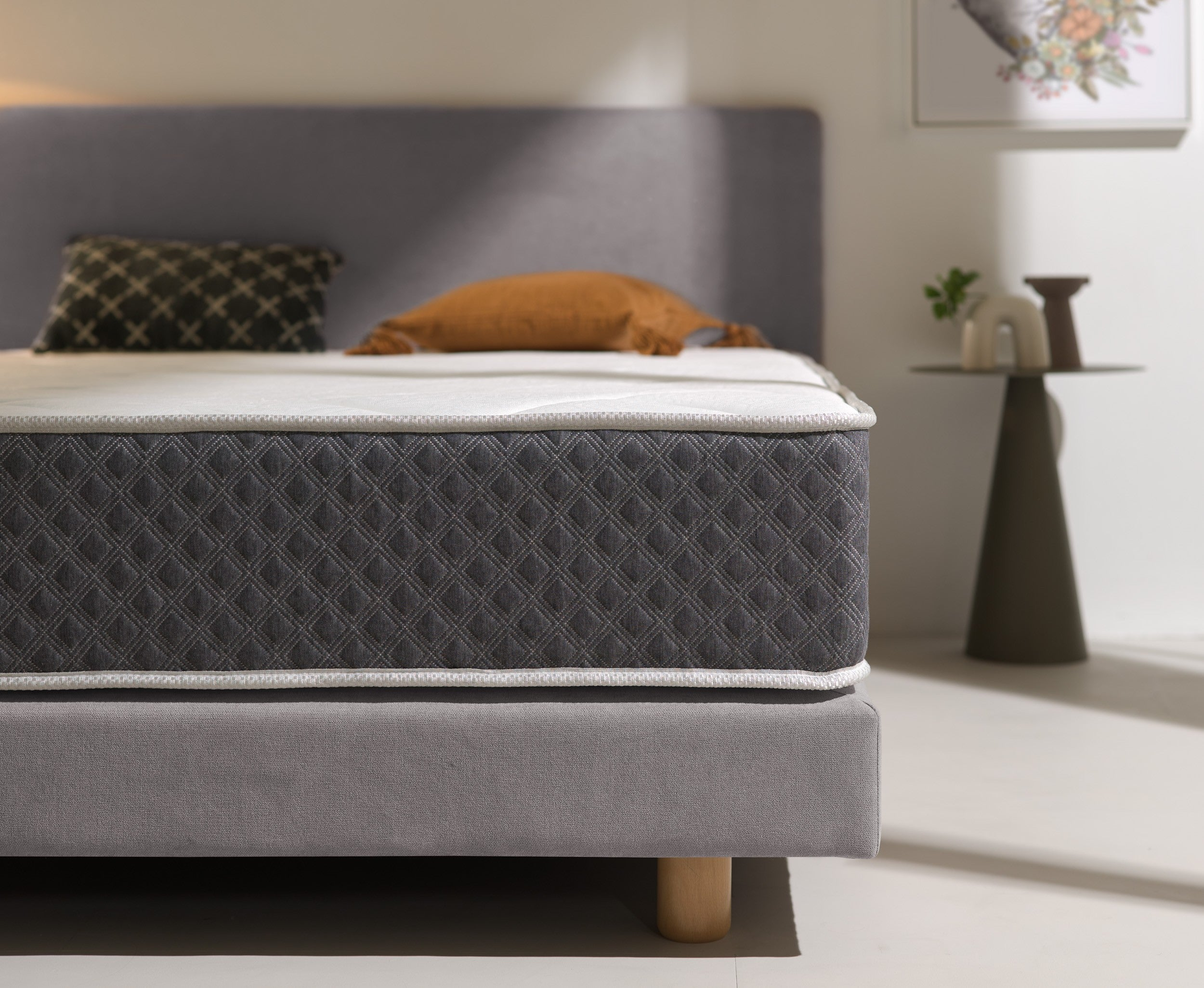 Dormitorio con cama, mesita de noche y lámpara. La cama tiene un cabecero gris.