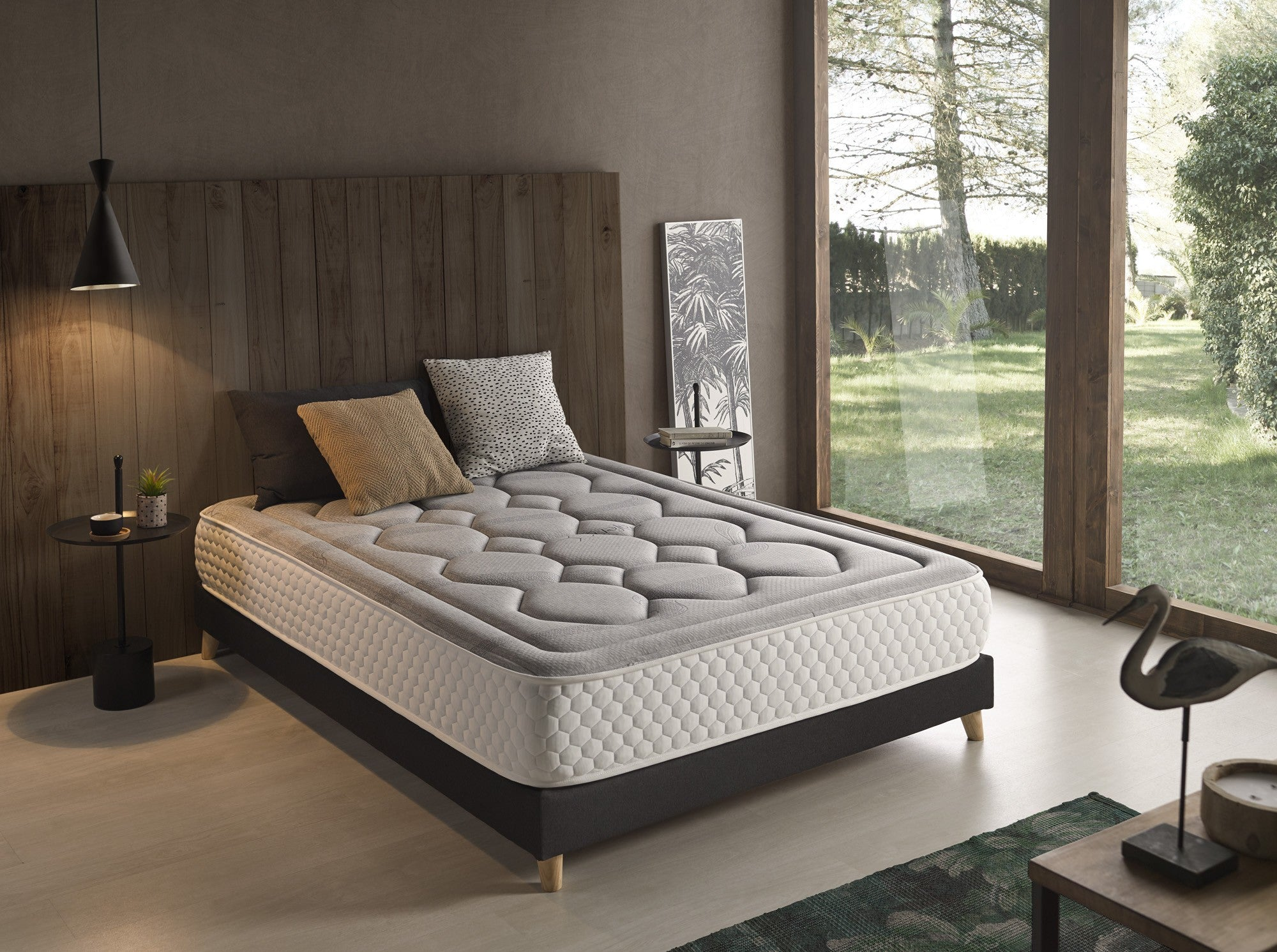 Dormitorio con cama de colchón gris, paneles de madera oscura y vista a la naturaleza.
